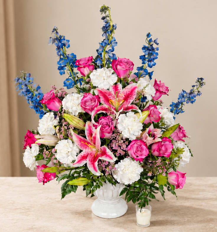 Pink roses, white lilies, and blue flowers in a white vase