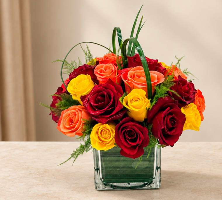 Bouquet of red, yellow, and orange roses in a square glass vase