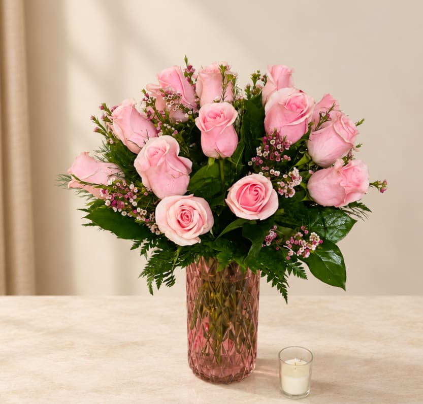 Pink roses arranged in a textured glass vase with a small candle nearby.