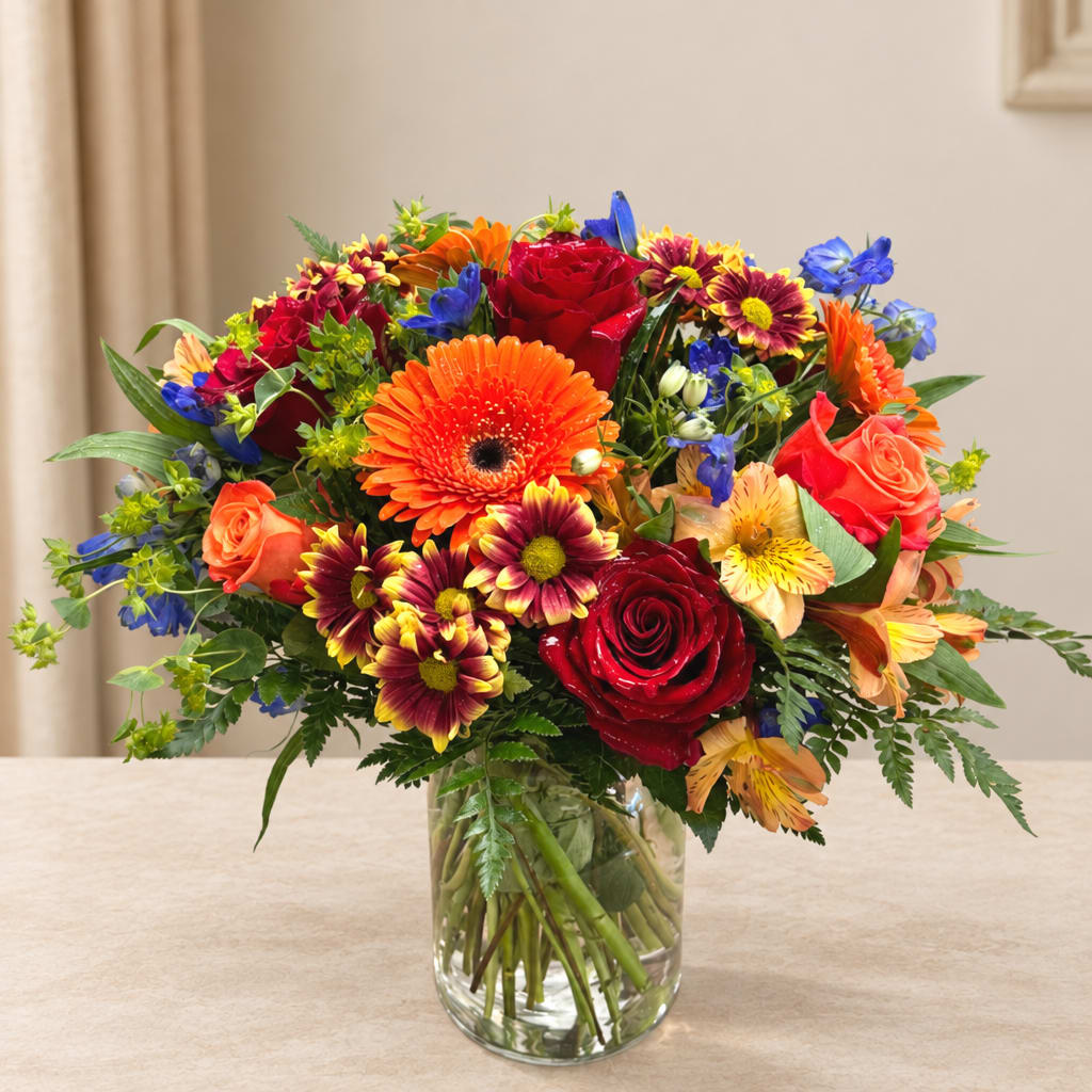Mixed bouquet of red, orange, yellow, and blue flowers in a clear glass vase