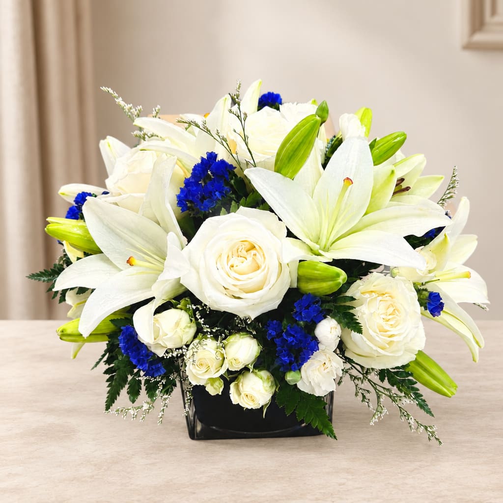 White lilies and roses with blue accents in a black square vase