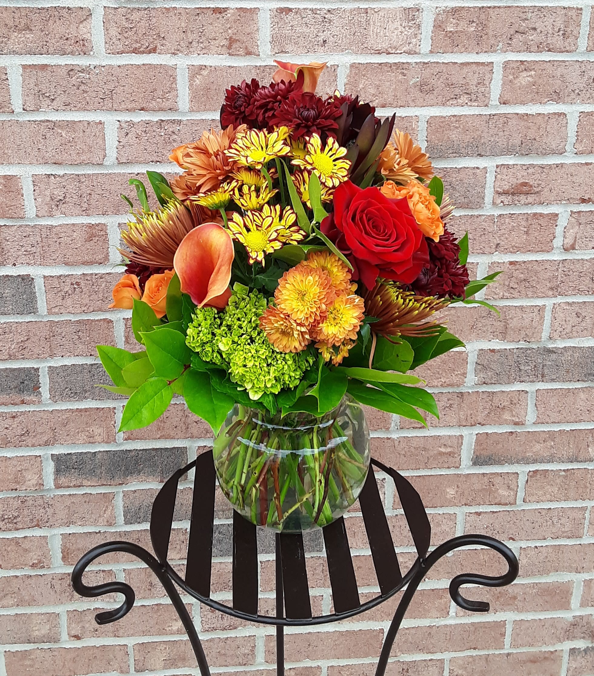 Mixed bouquet of red, orange, and yellow flowers in a clear glass vase