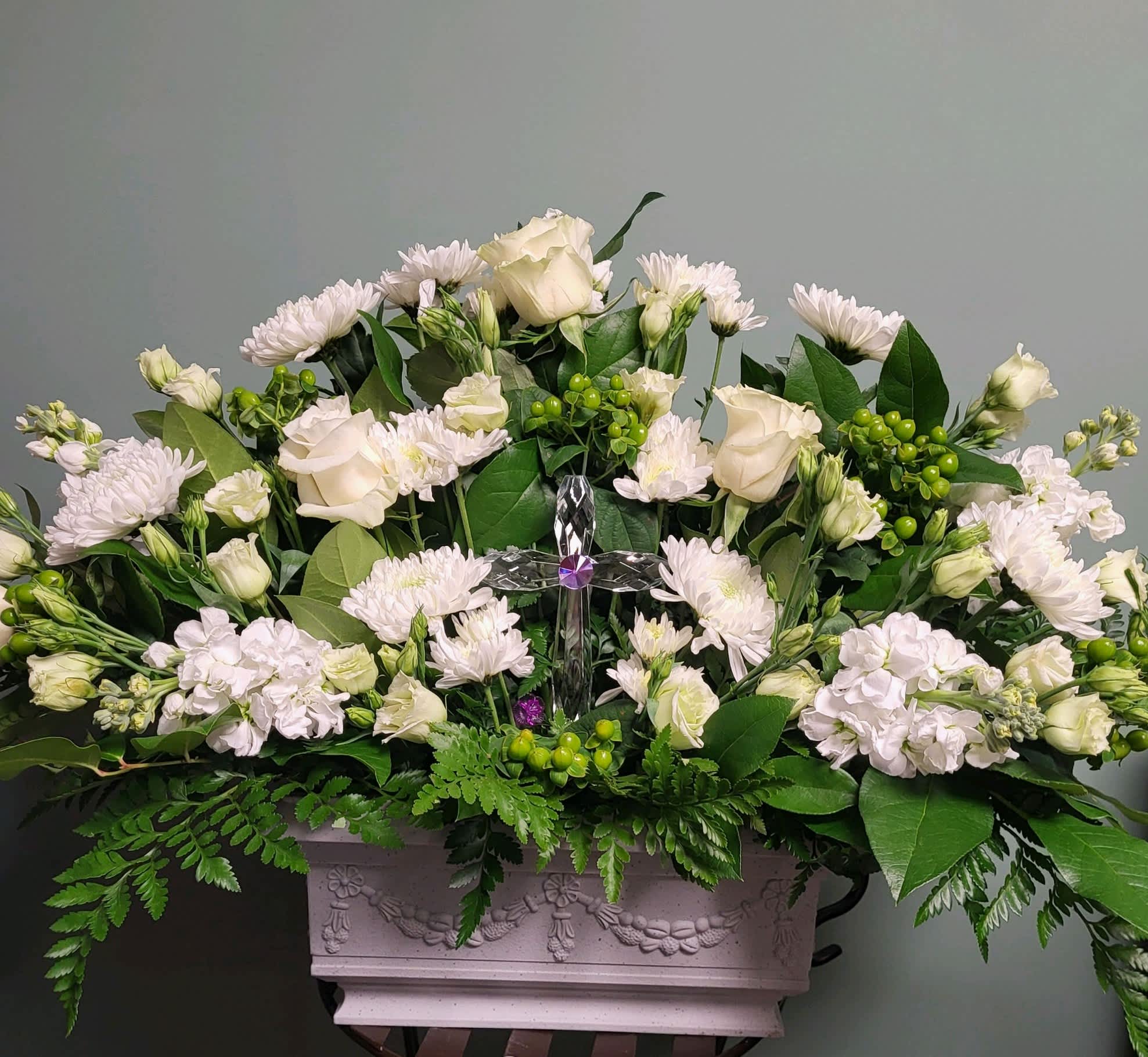 White floral arrangement in a decorative rectangular planter with a clear cross centerpiece