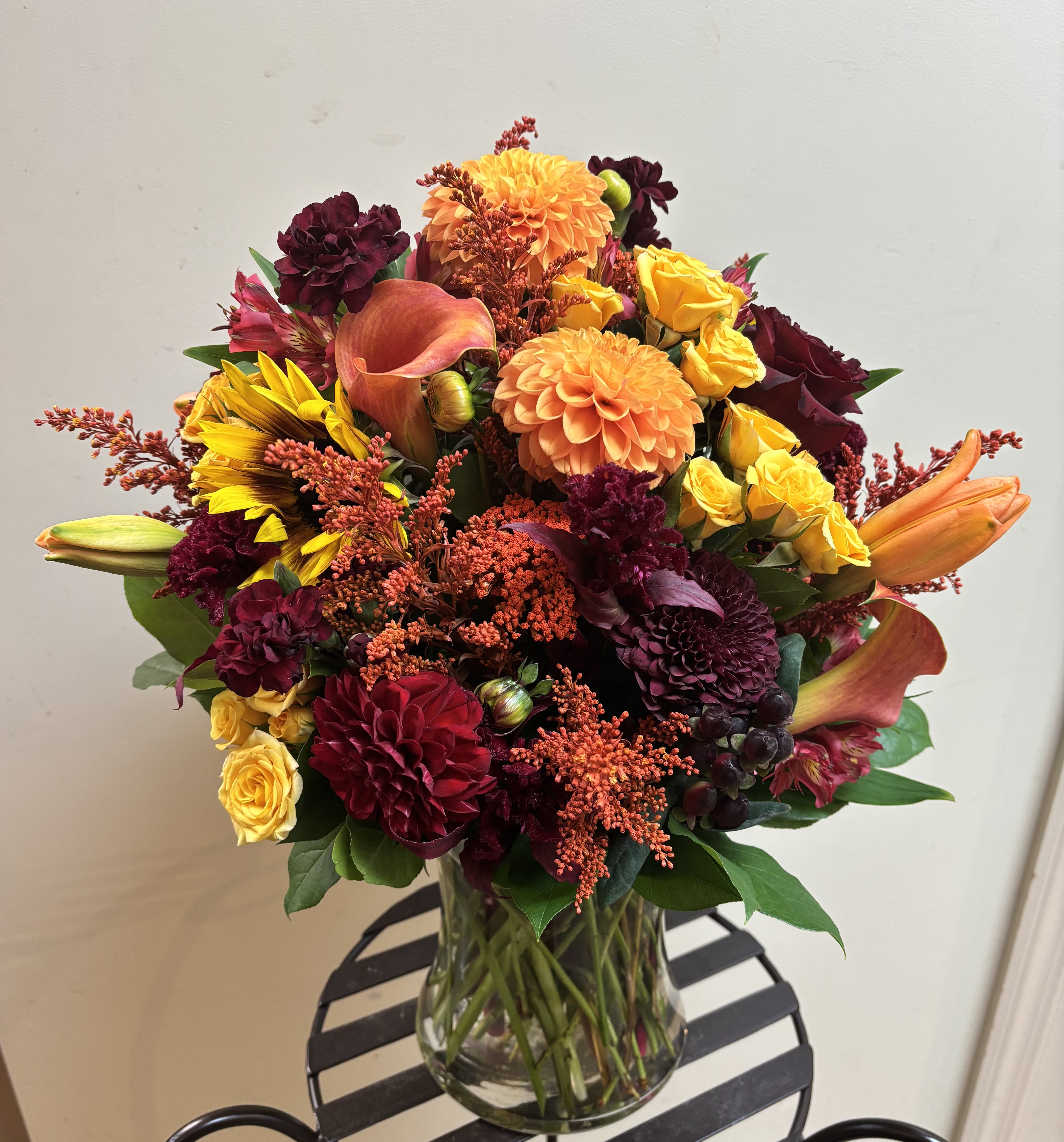 Bouquet of orange, yellow, and burgundy flowers in a clear glass vase