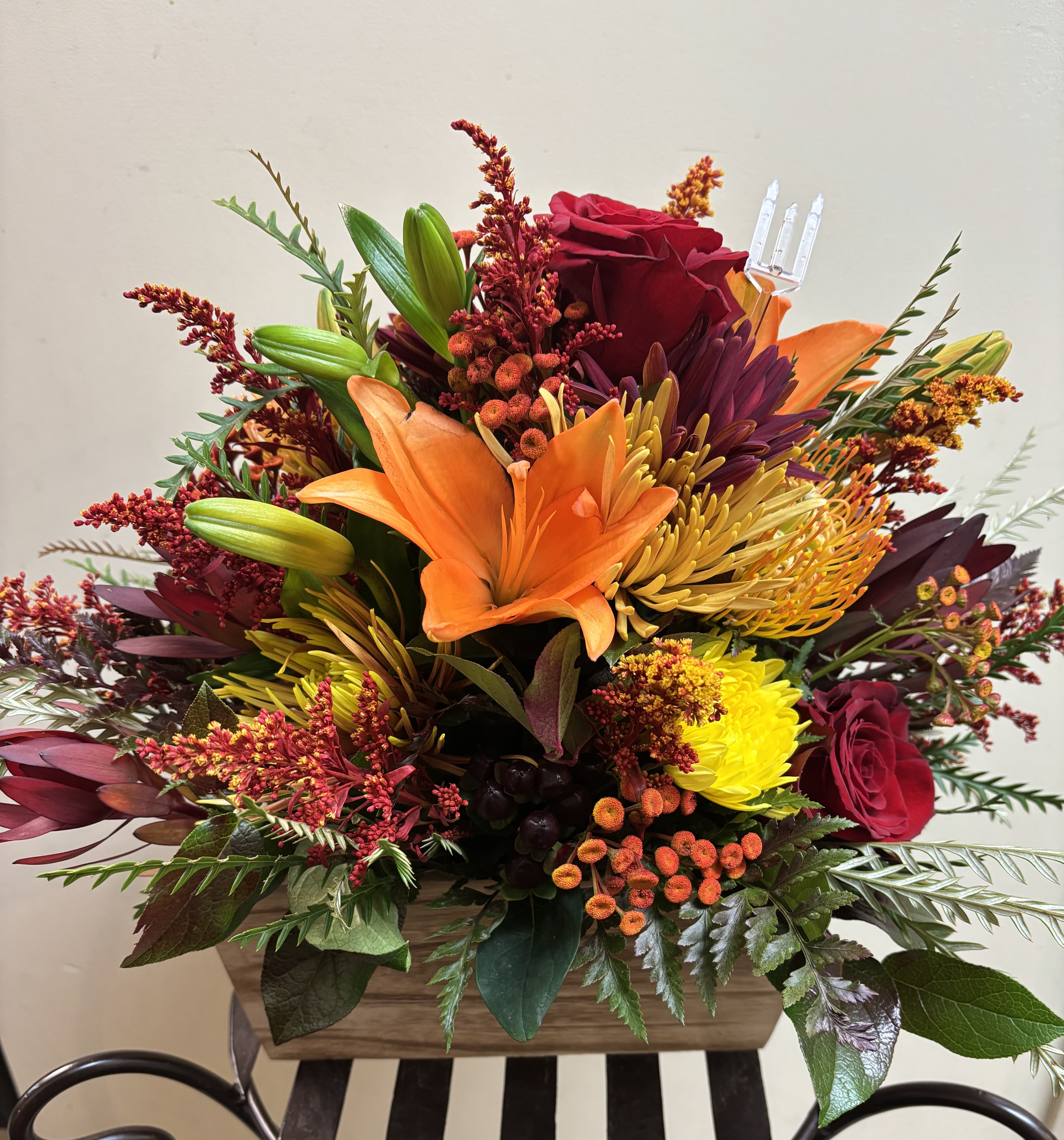 Mixed bouquet with orange lilies, red roses, and yellow chrysanthemums in a wooden container
