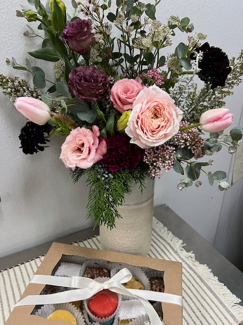 Mixed pink and burgundy bouquet in a tall vase with a box of macarons in front