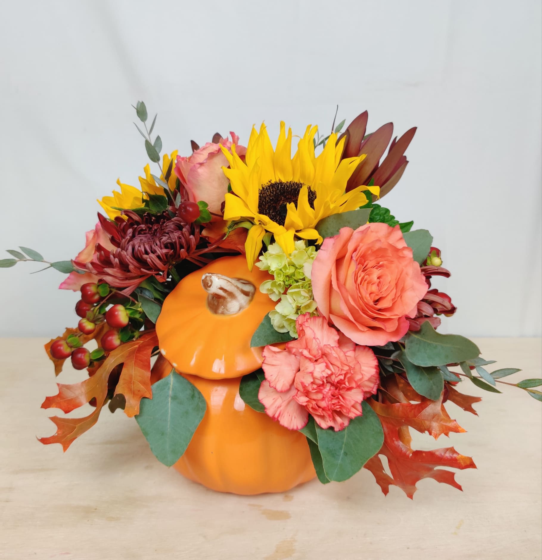 Fall floral arrangement in an orange pumpkin container with sunflowers and roses