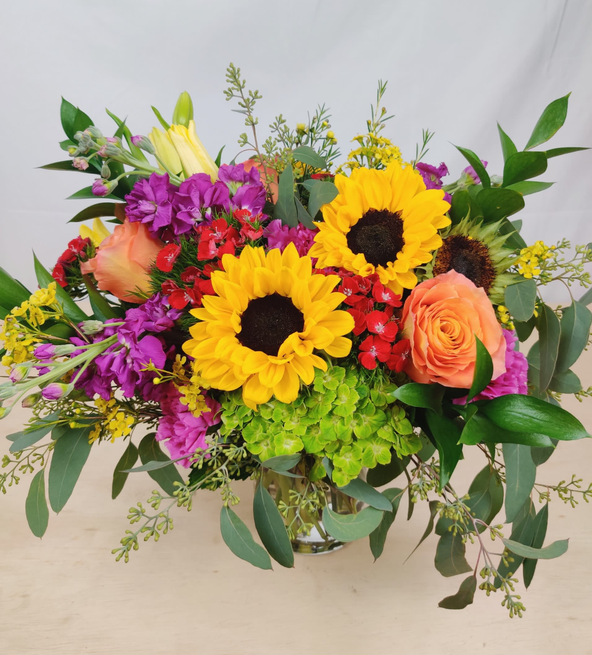 Bouquet of sunflowers, peach roses, and purple flowers in a glass vase