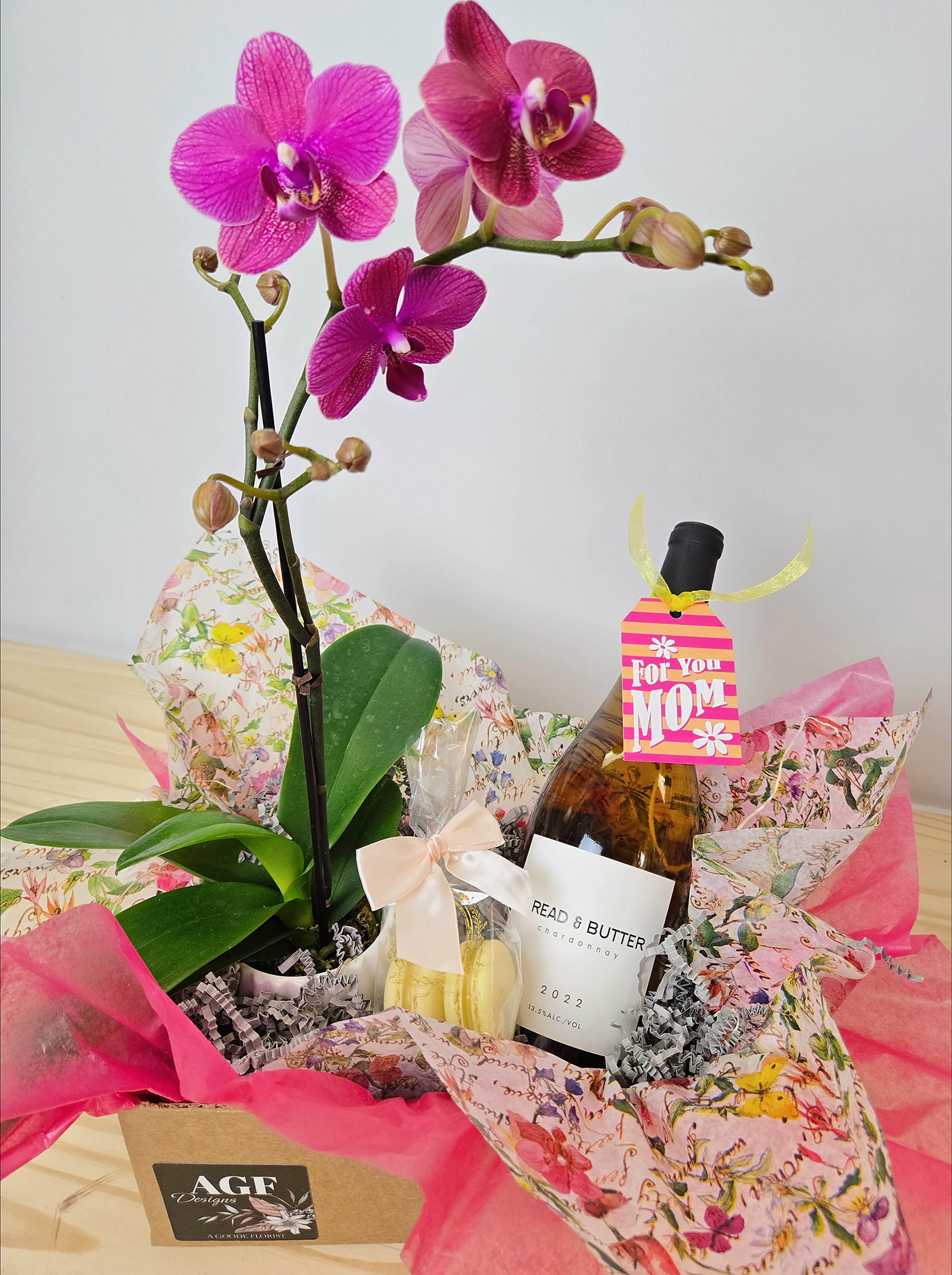 Pink orchid plant in a gift basket with a bottle and wrapped treats