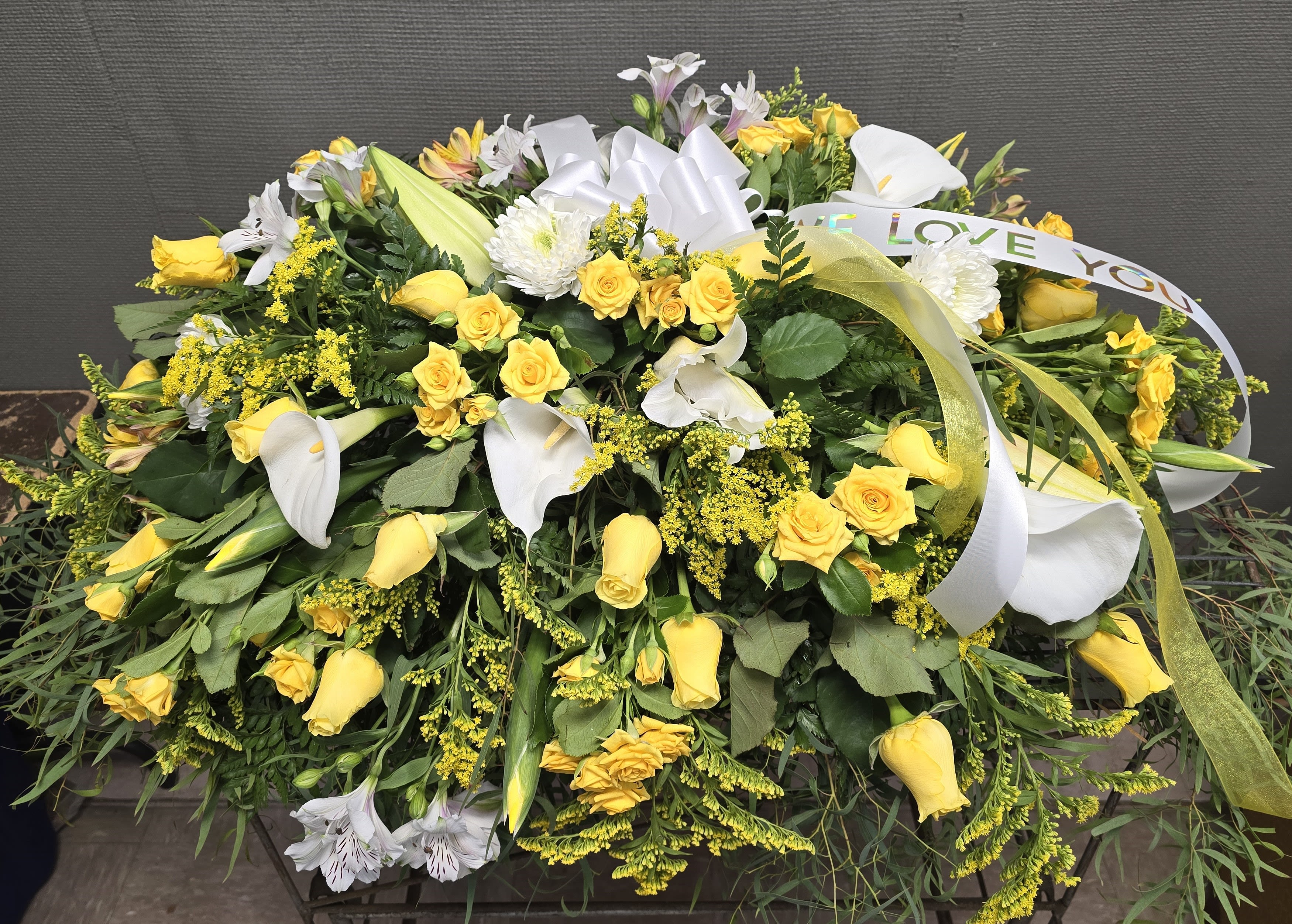 Yellow roses and white lilies arranged in a large sympathy spray with ribbon