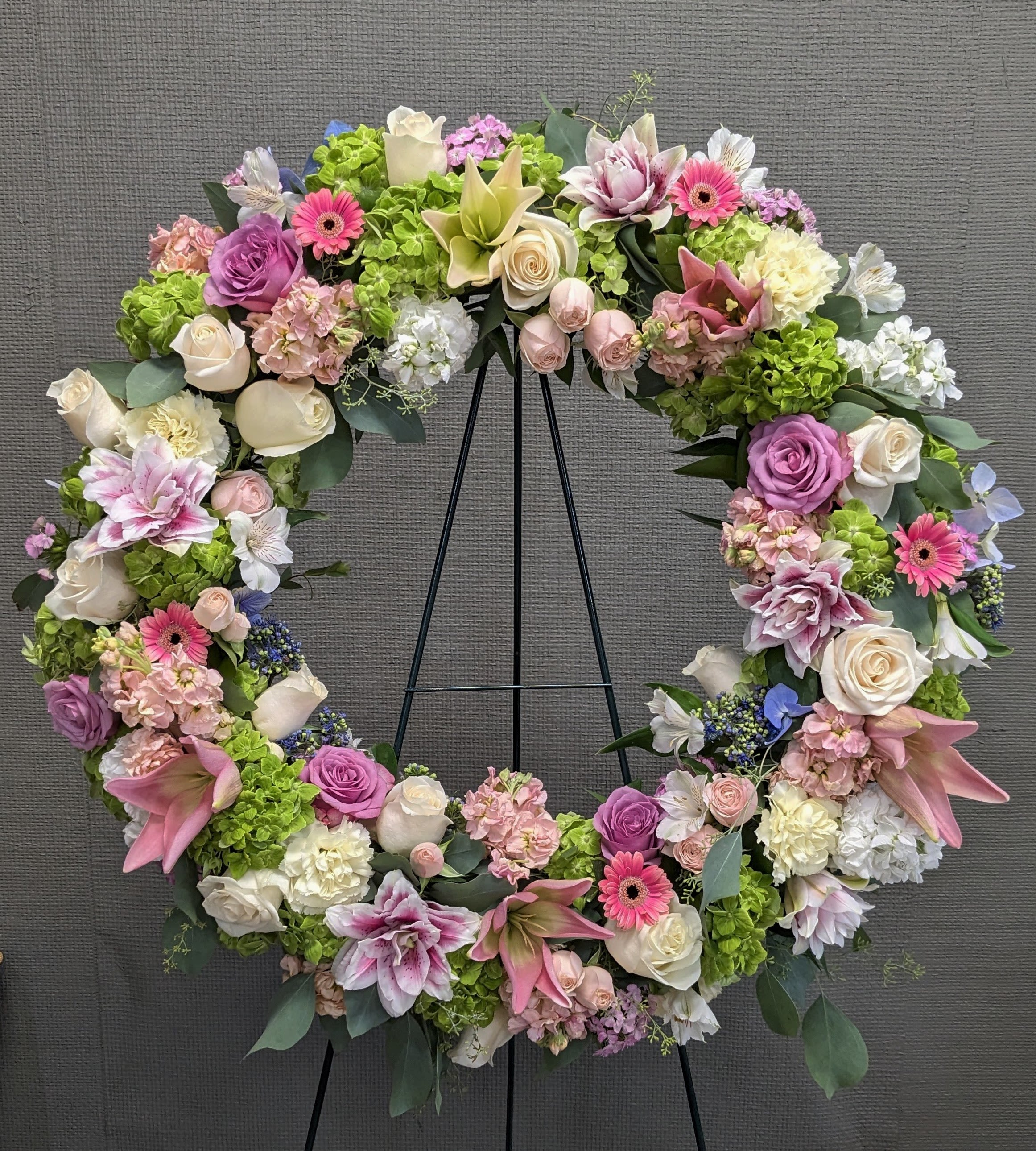 Large floral wreath with pink, white, and green flowers on a black stand