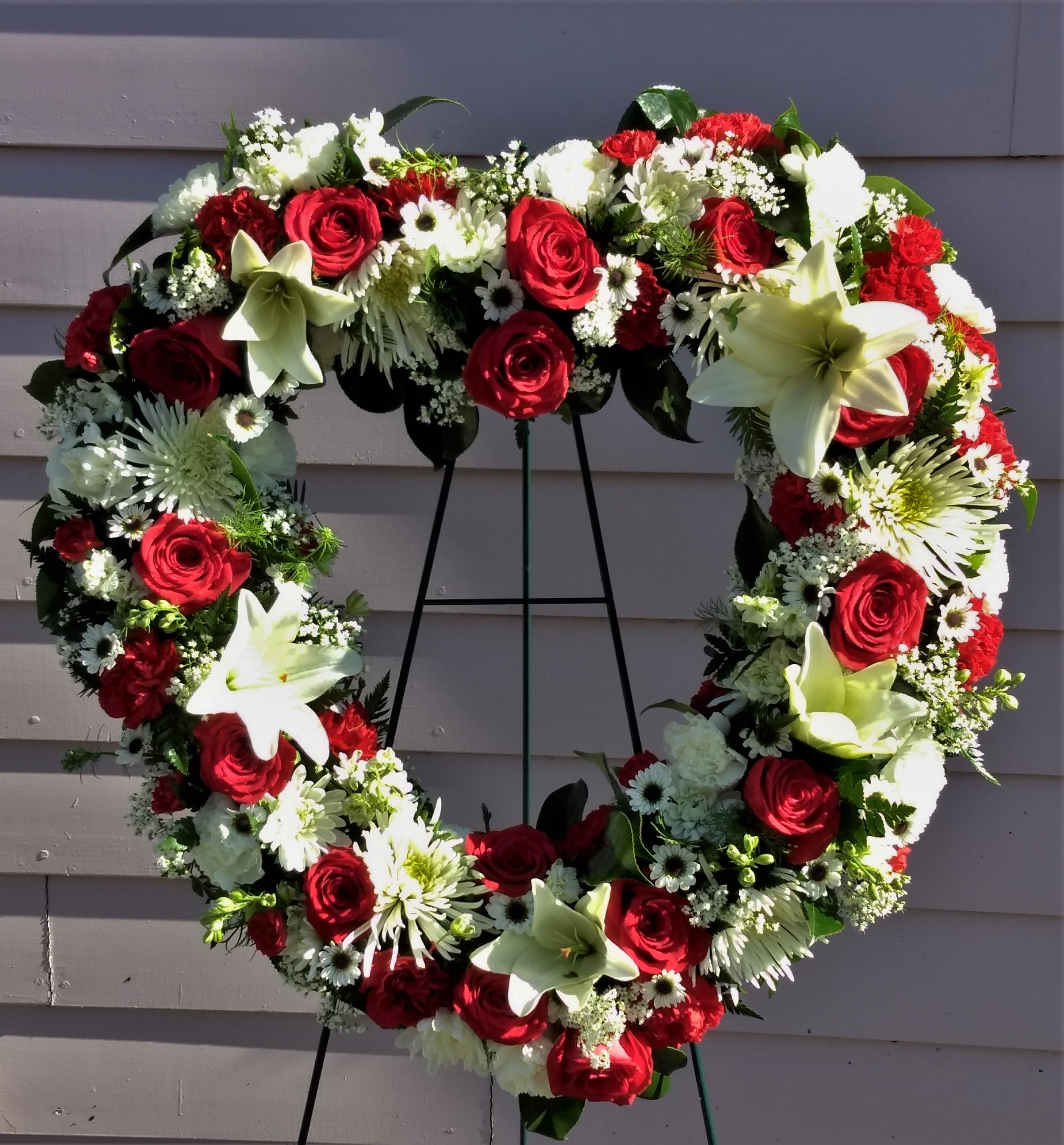 Heart-shaped floral wreath with red roses and white lilies on an easel