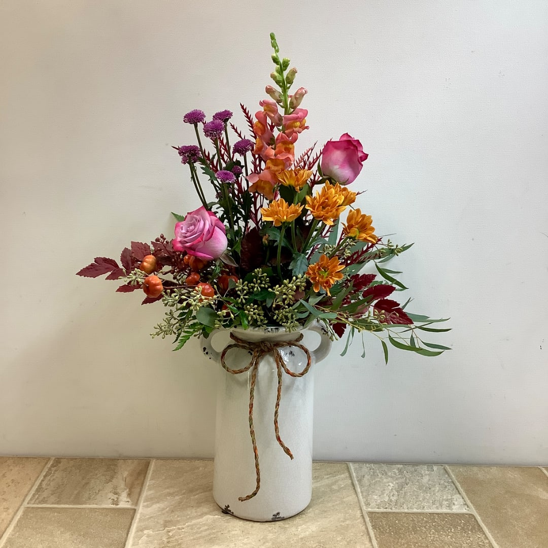 Pink roses and mixed flowers arranged in a white vase with a rope bow