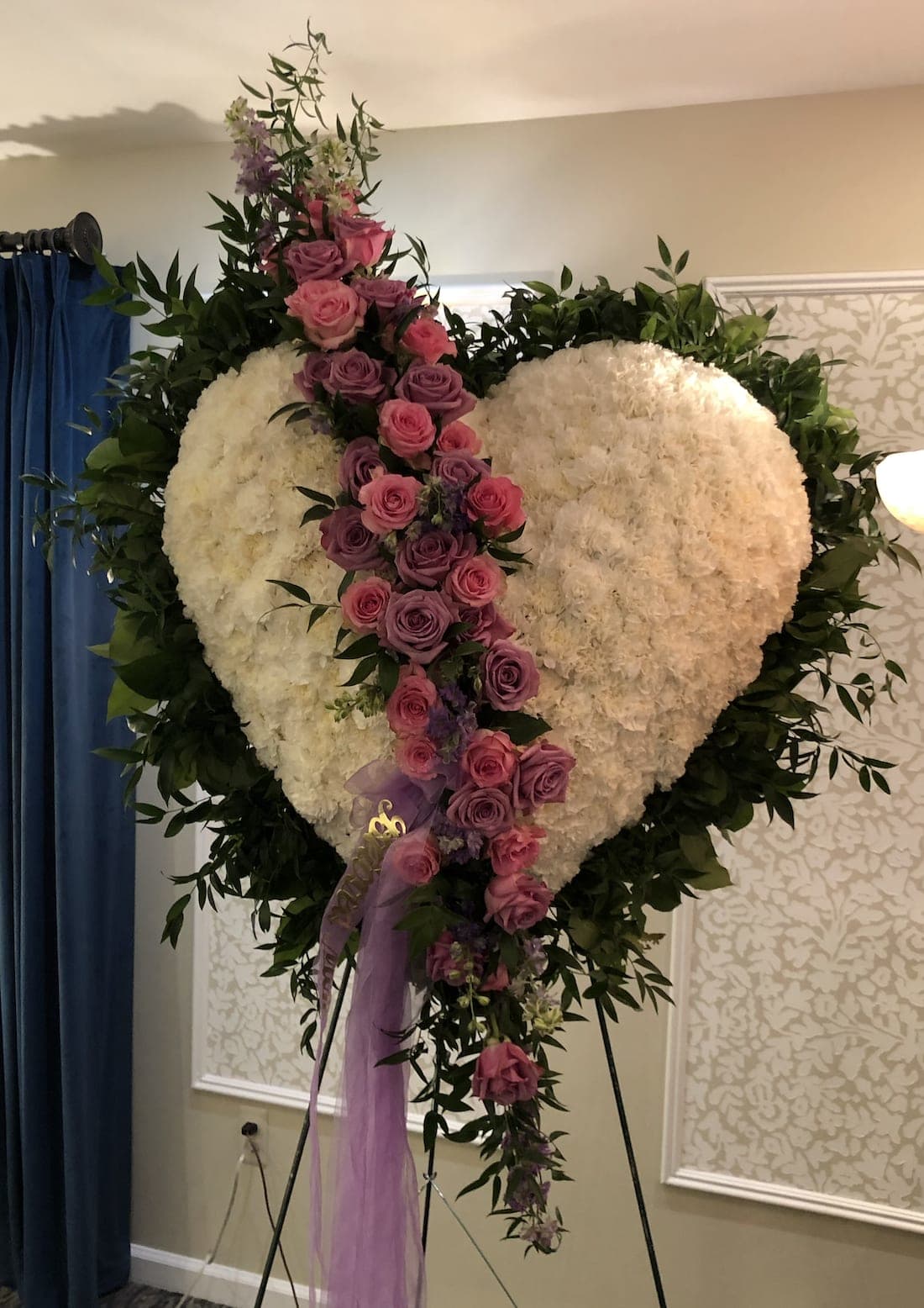 Heart-shaped floral tribute with pink and purple roses on an easel