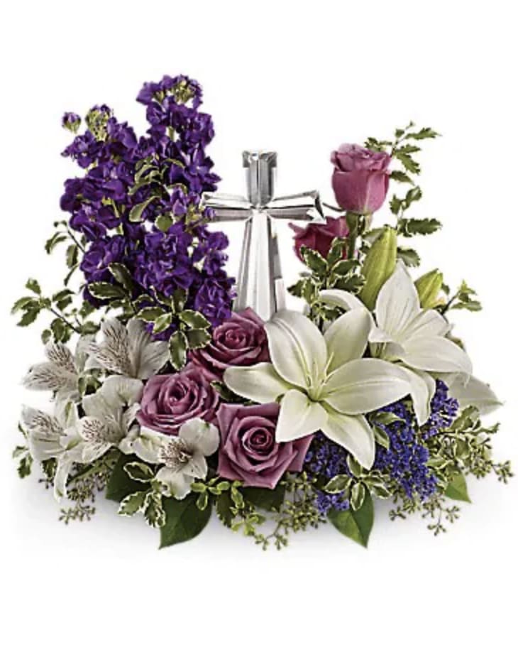 Purple roses and white lilies arranged around a silver cross