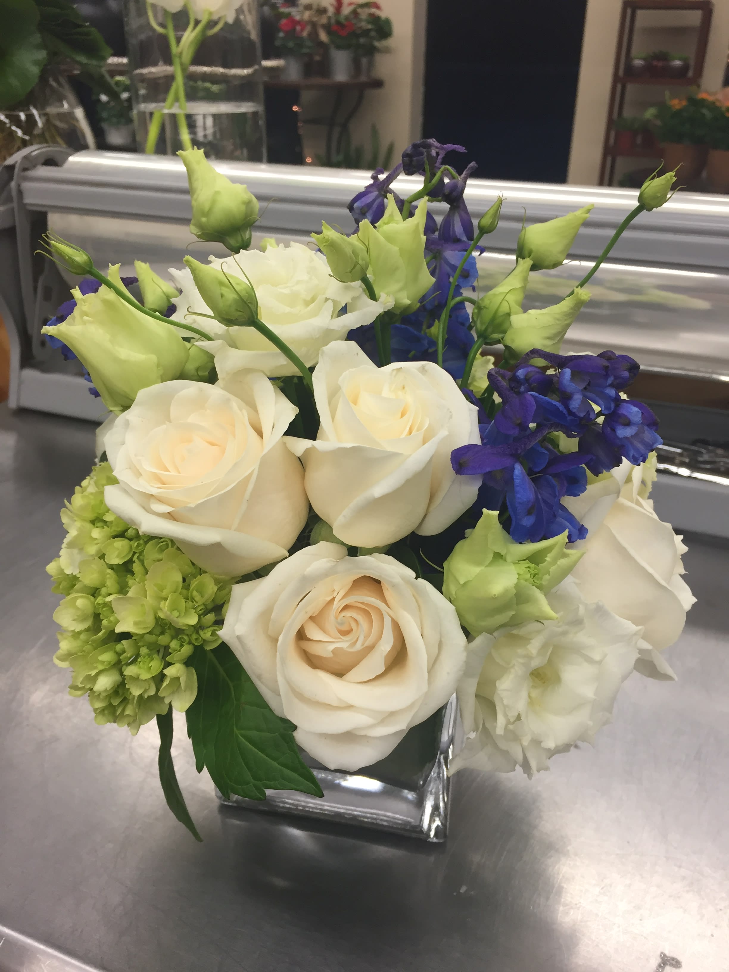 Cream roses and blue flowers arranged in a square glass vase