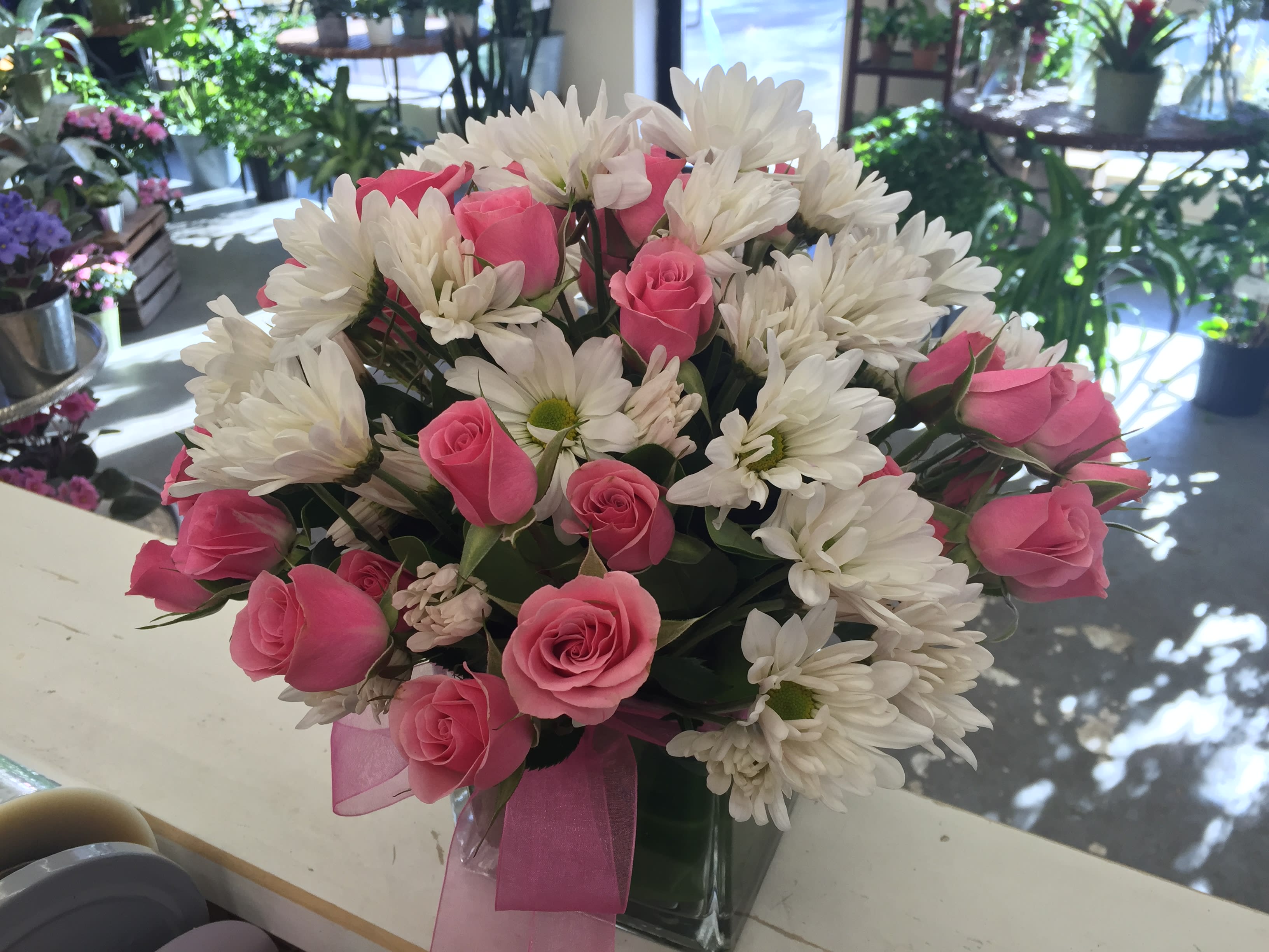 Pink roses and white daisies arranged in a clear vase with a pink ribbon.