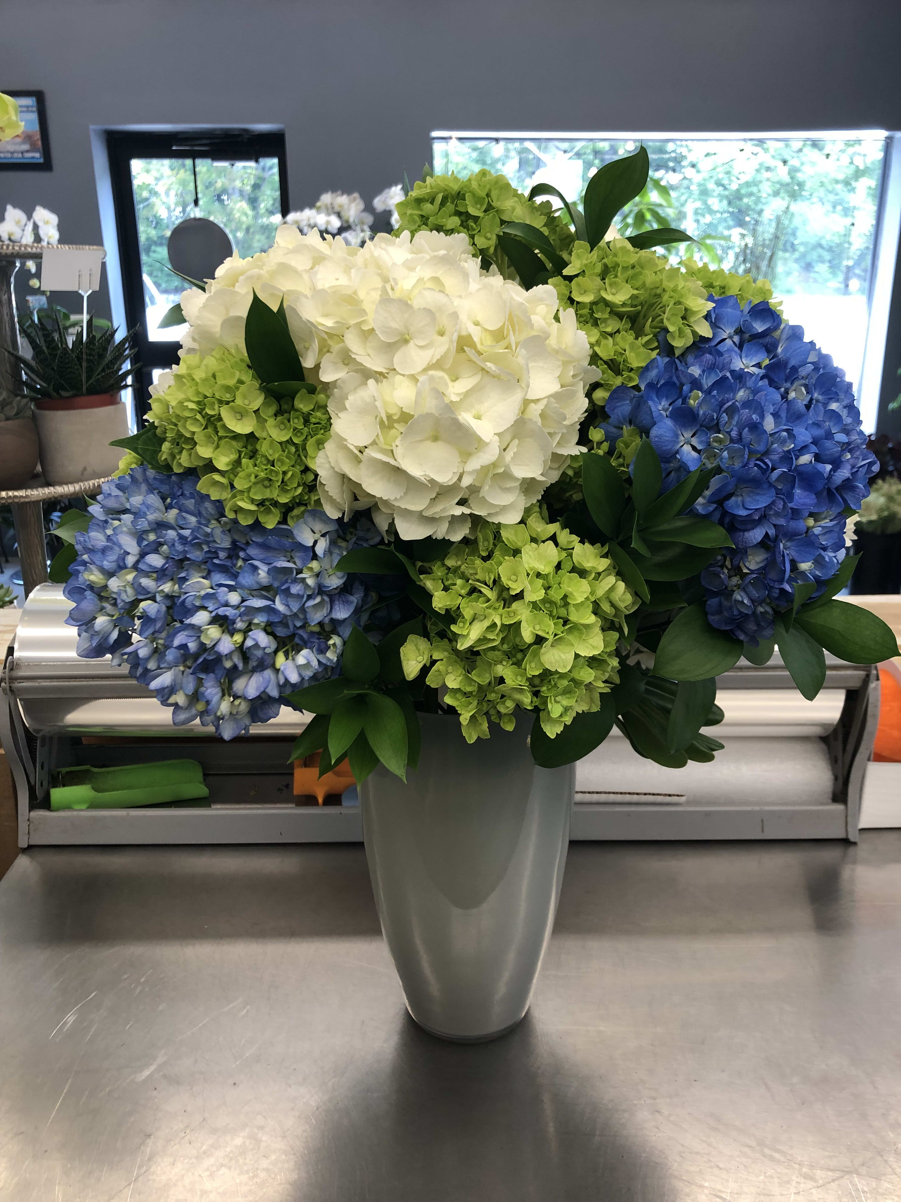 Blue, green, and white hydrangea arrangement in a tall gray vase