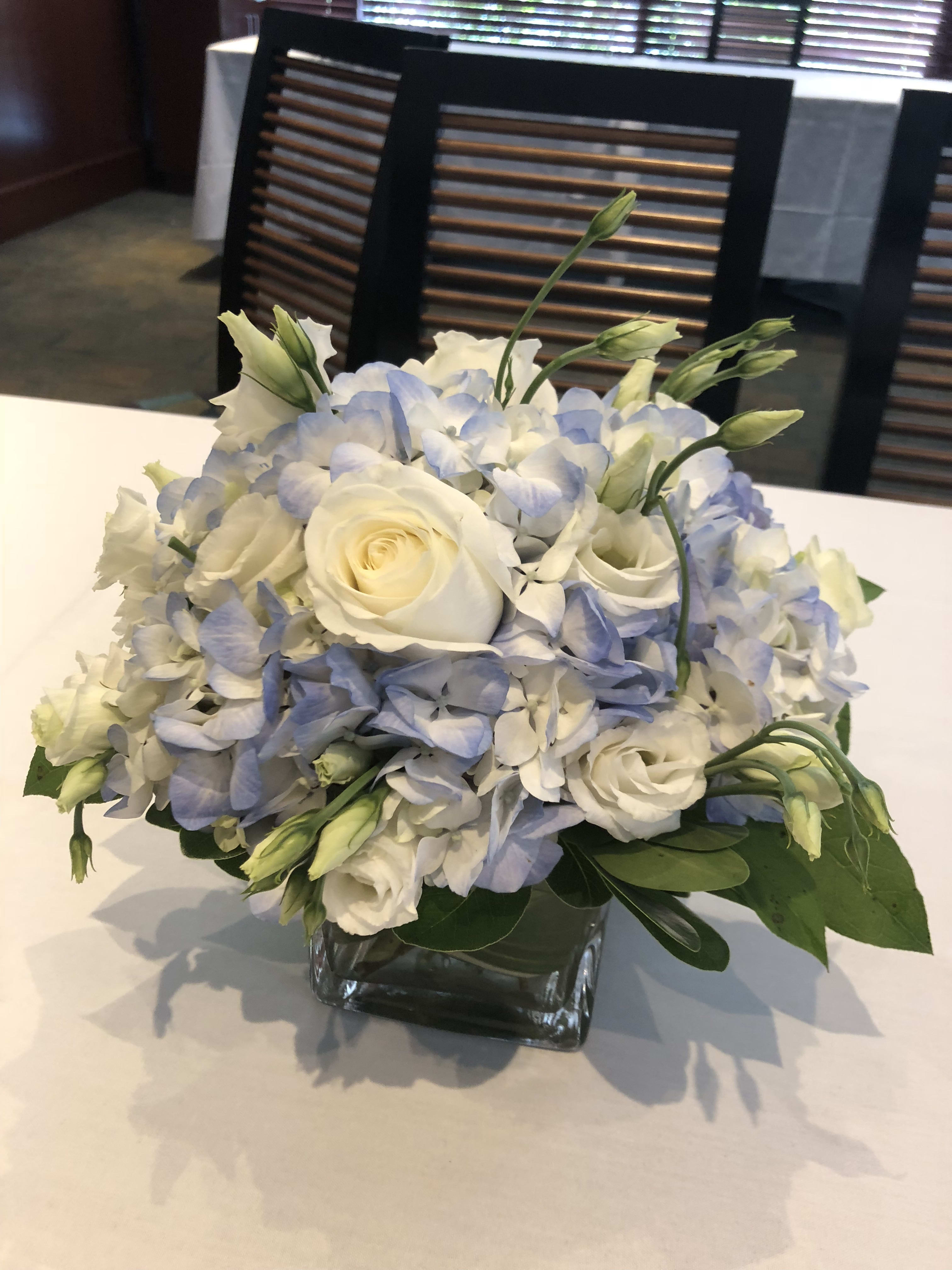 White roses and pale blue hydrangeas in a square glass vase