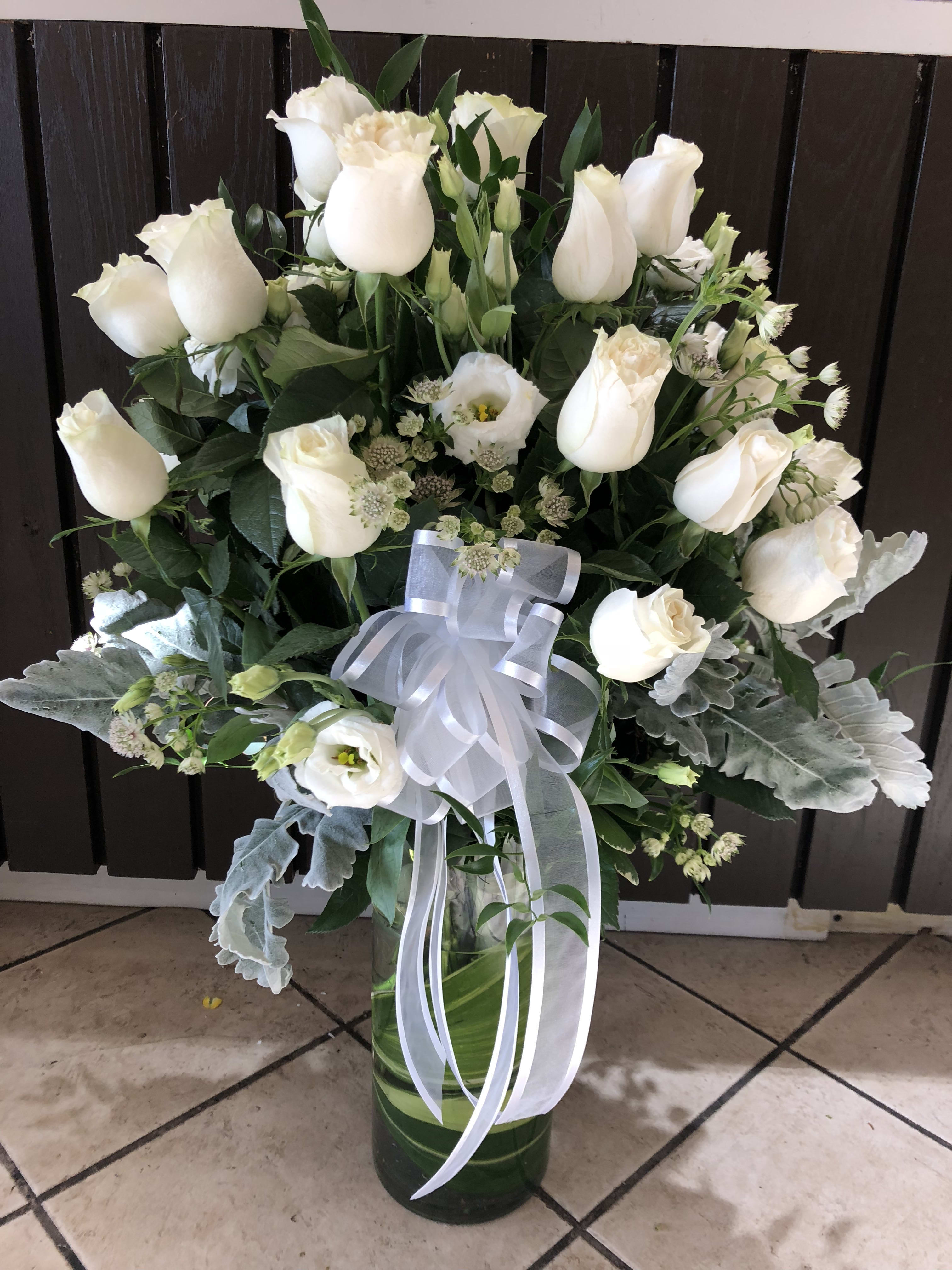 White roses and lisianthus in a glass vase with a white ribbon