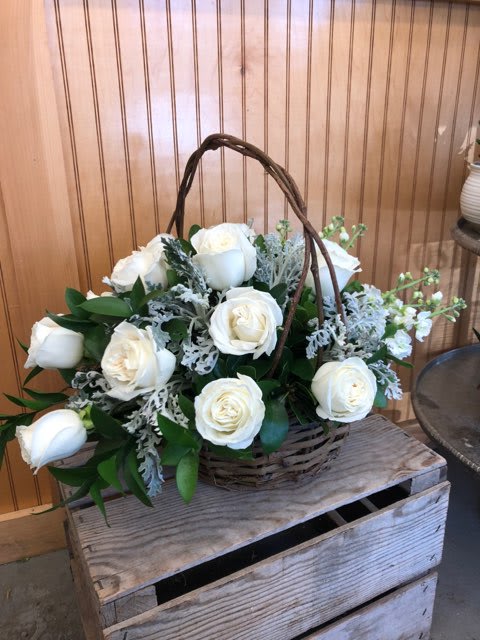 White roses in a wicker basket with greenery