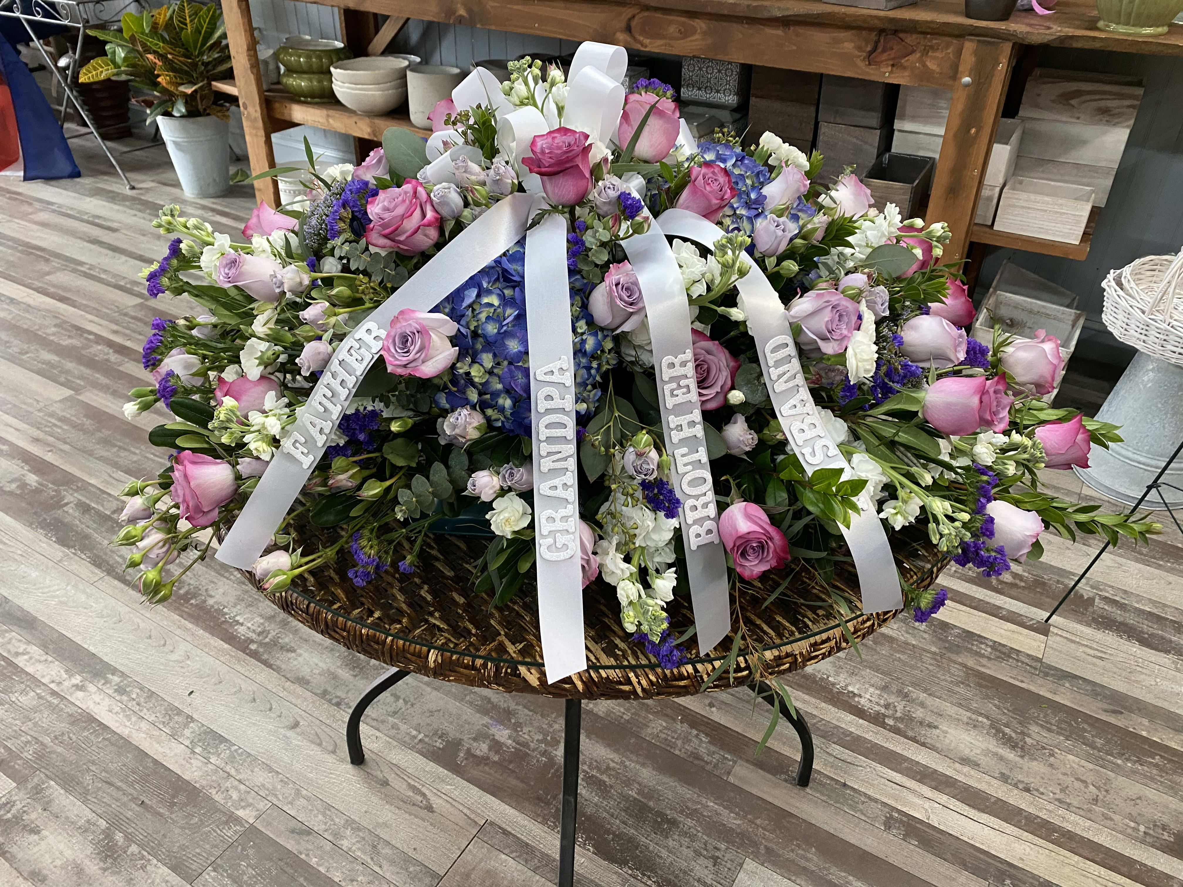 Large sympathy floral arrangement with pink and purple roses and white ribbons