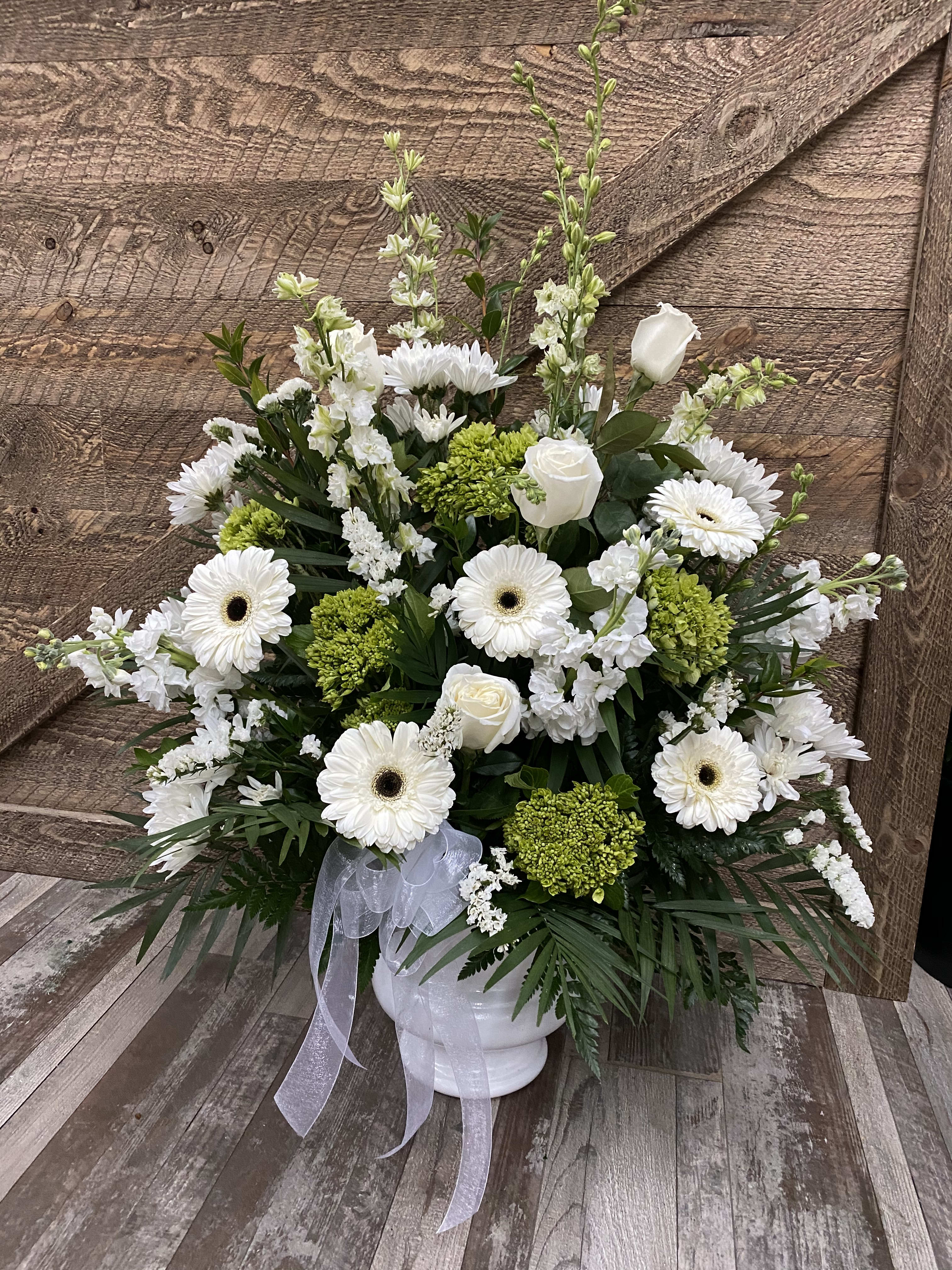 White and green floral arrangement in a white vase with a ribbon