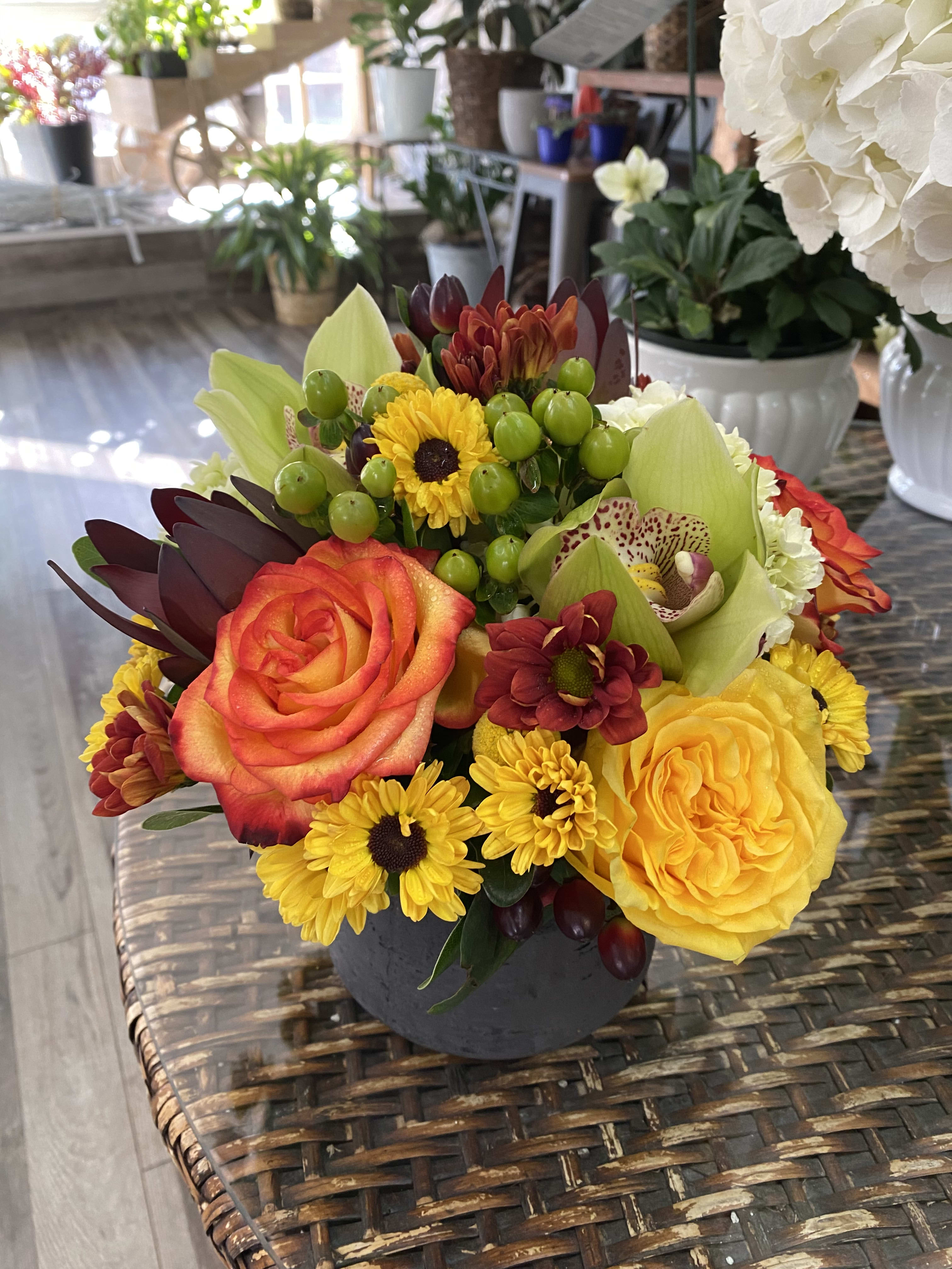 Mixed bouquet with roses, orchids, and yellow daisies in a dark vase