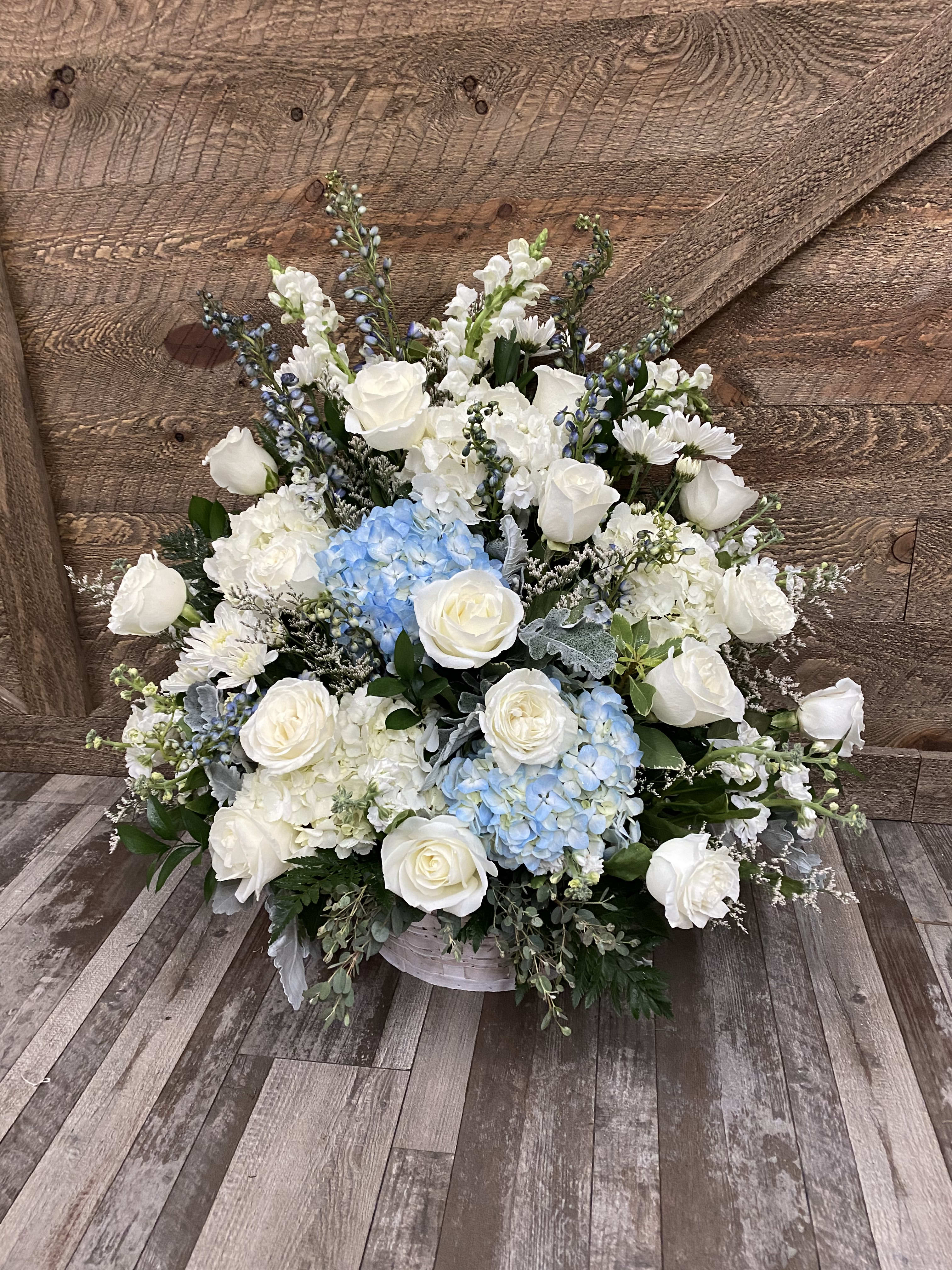 Large white floral arrangement with blue hydrangeas in a low container