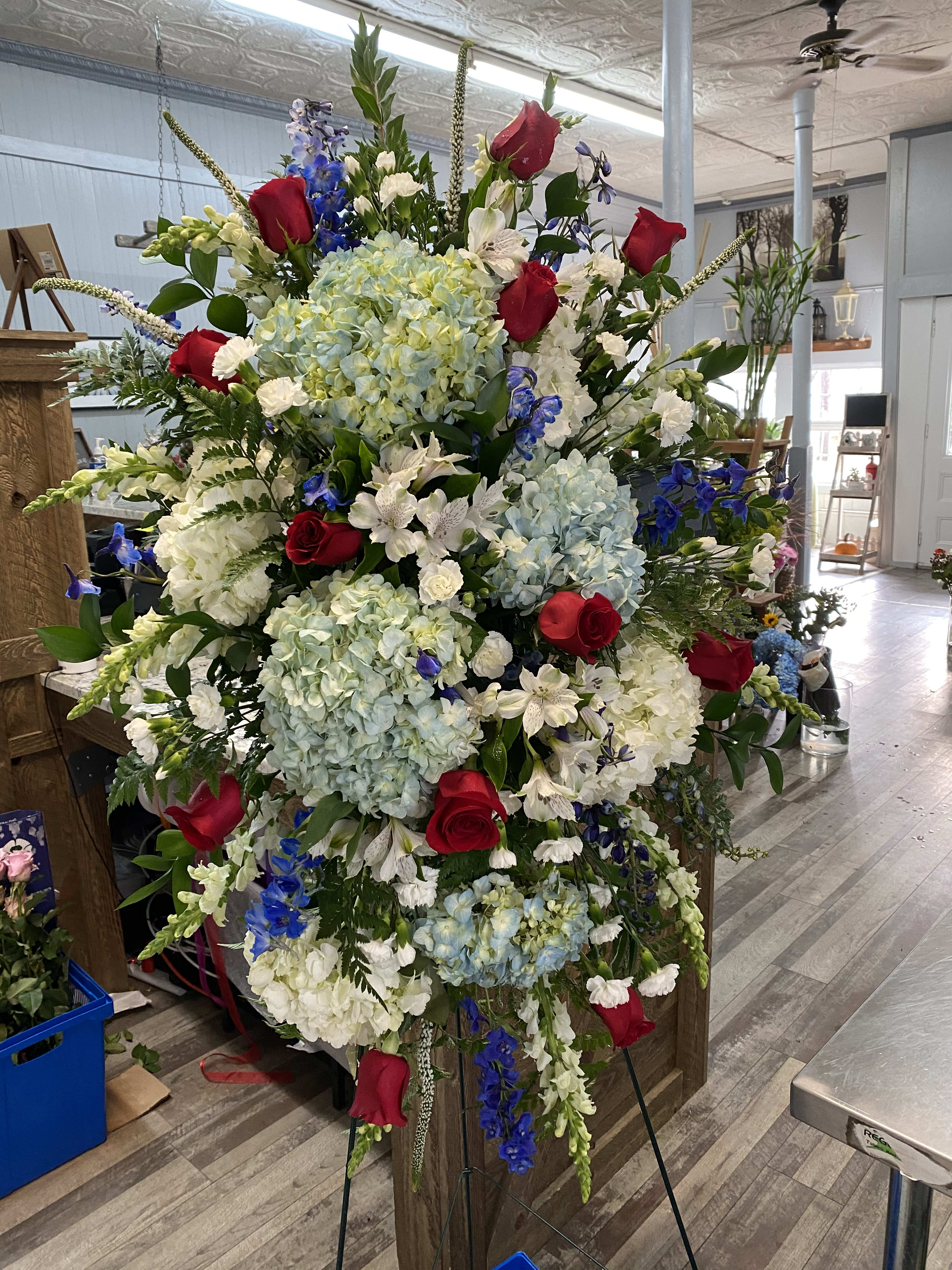 Large standing floral spray with red roses, blue hydrangeas, and white blooms