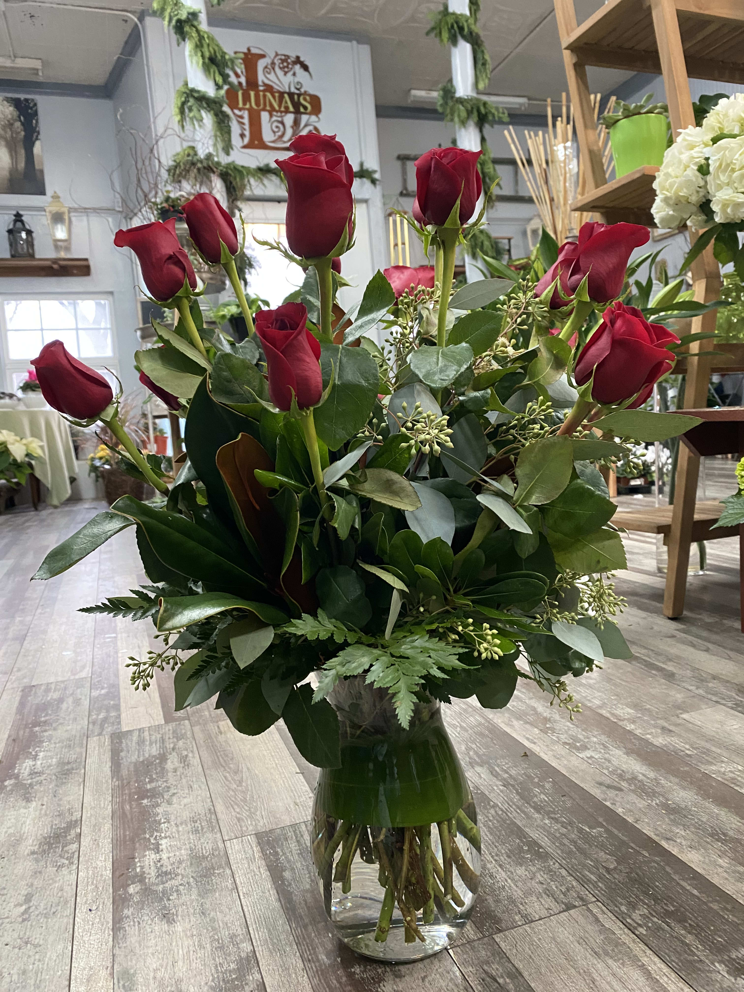 Red roses arranged in a clear glass vase with greenery