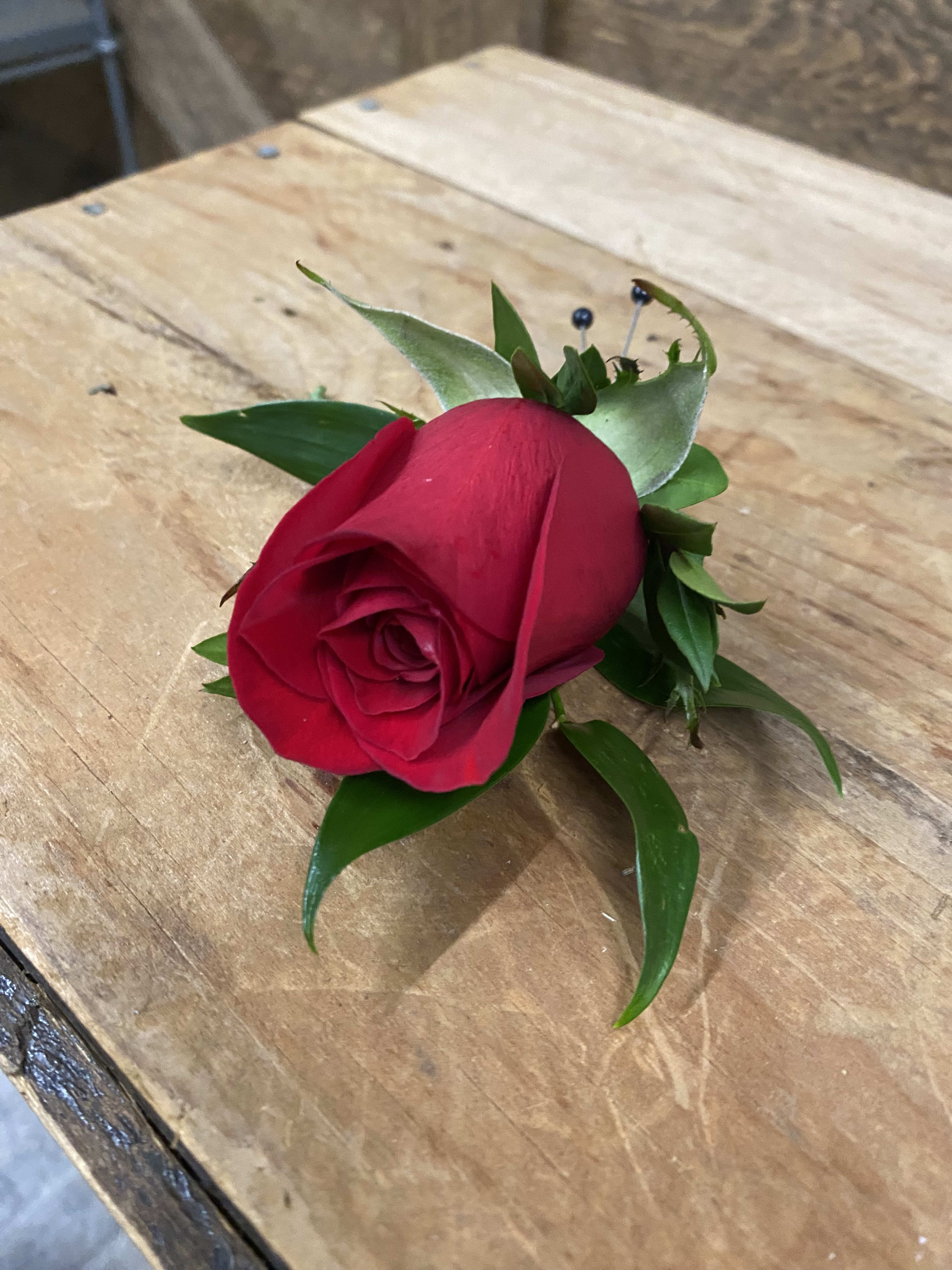 Single red rose boutonniere with green leaves on a wooden surface