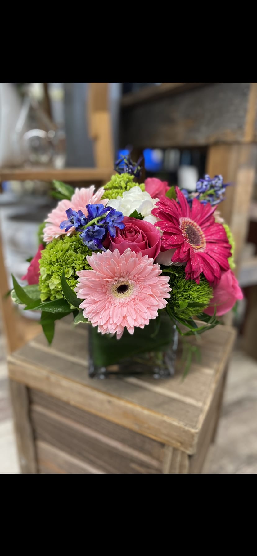 Mixed bouquet with pink gerbera daisies, roses, and blue flowers in a glass vase