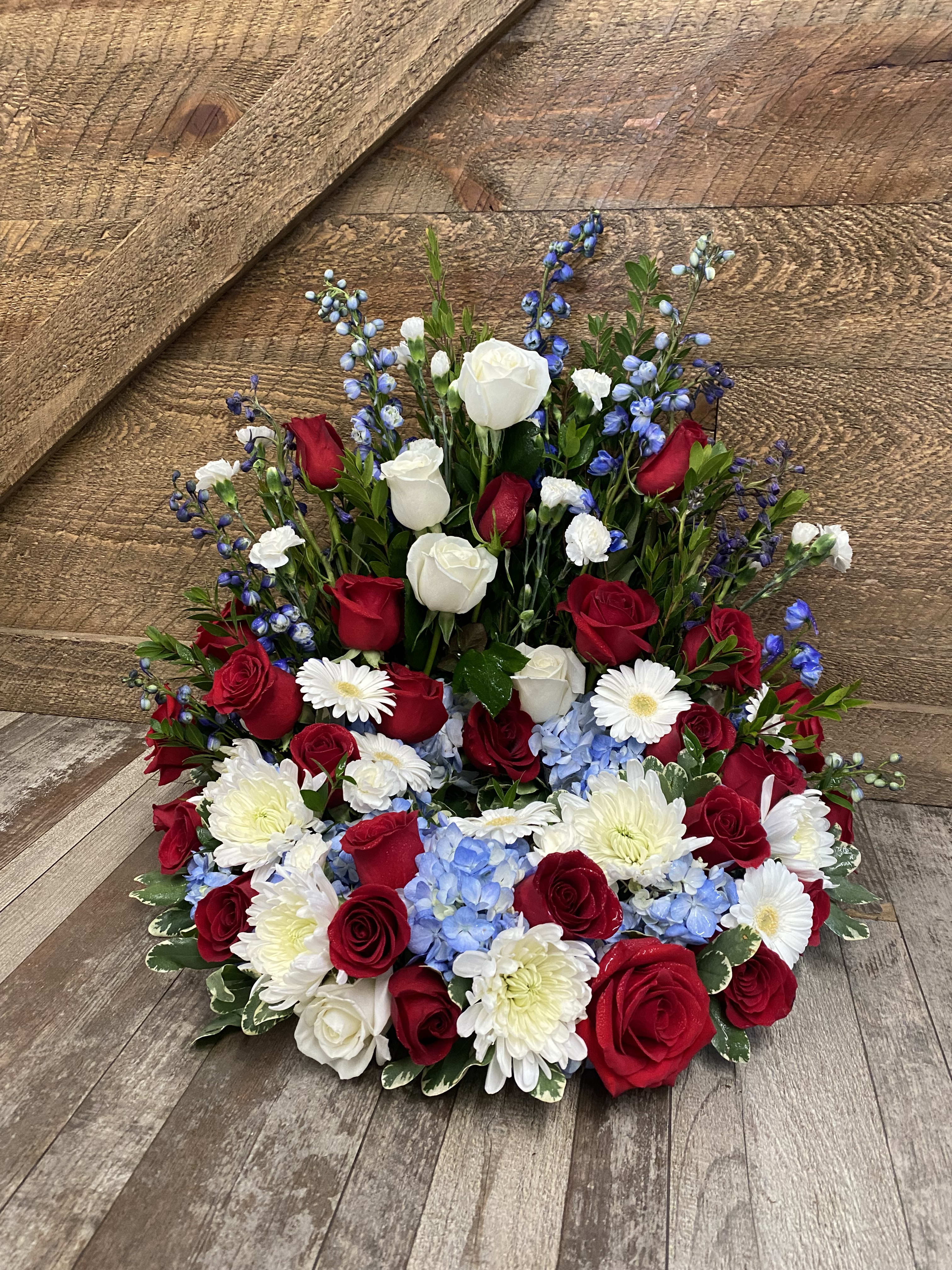 Red and white roses with blue flowers and white daisies in a low arrangement