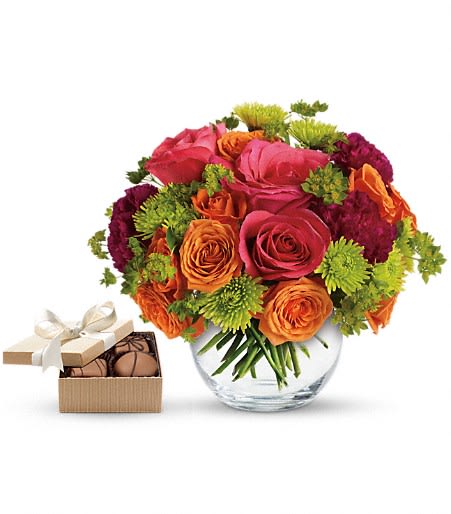 Bouquet of pink, orange, and green flowers in a glass vase with a box of chocolates