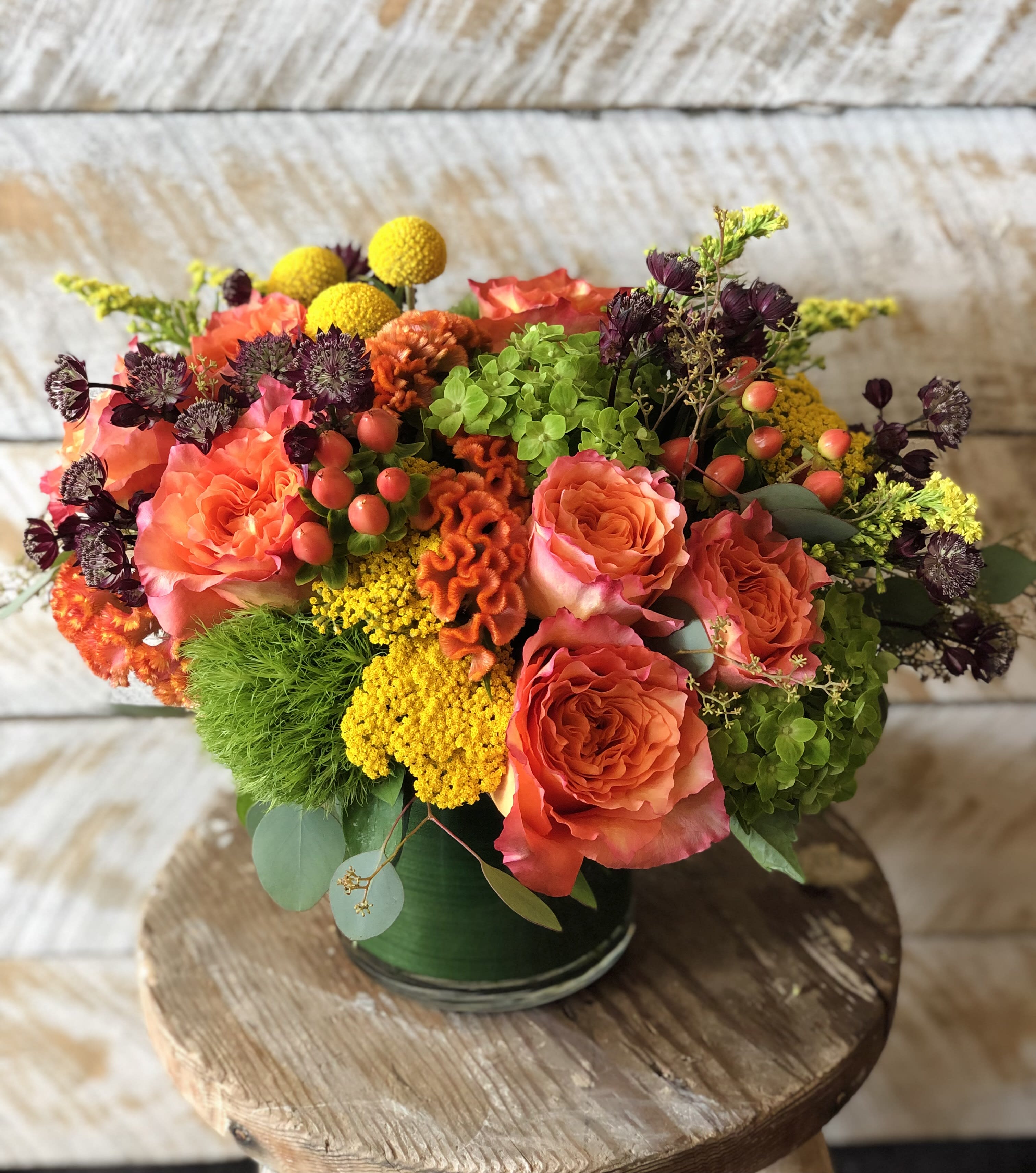 Mixed bouquet of orange roses and yellow blooms in a green vase