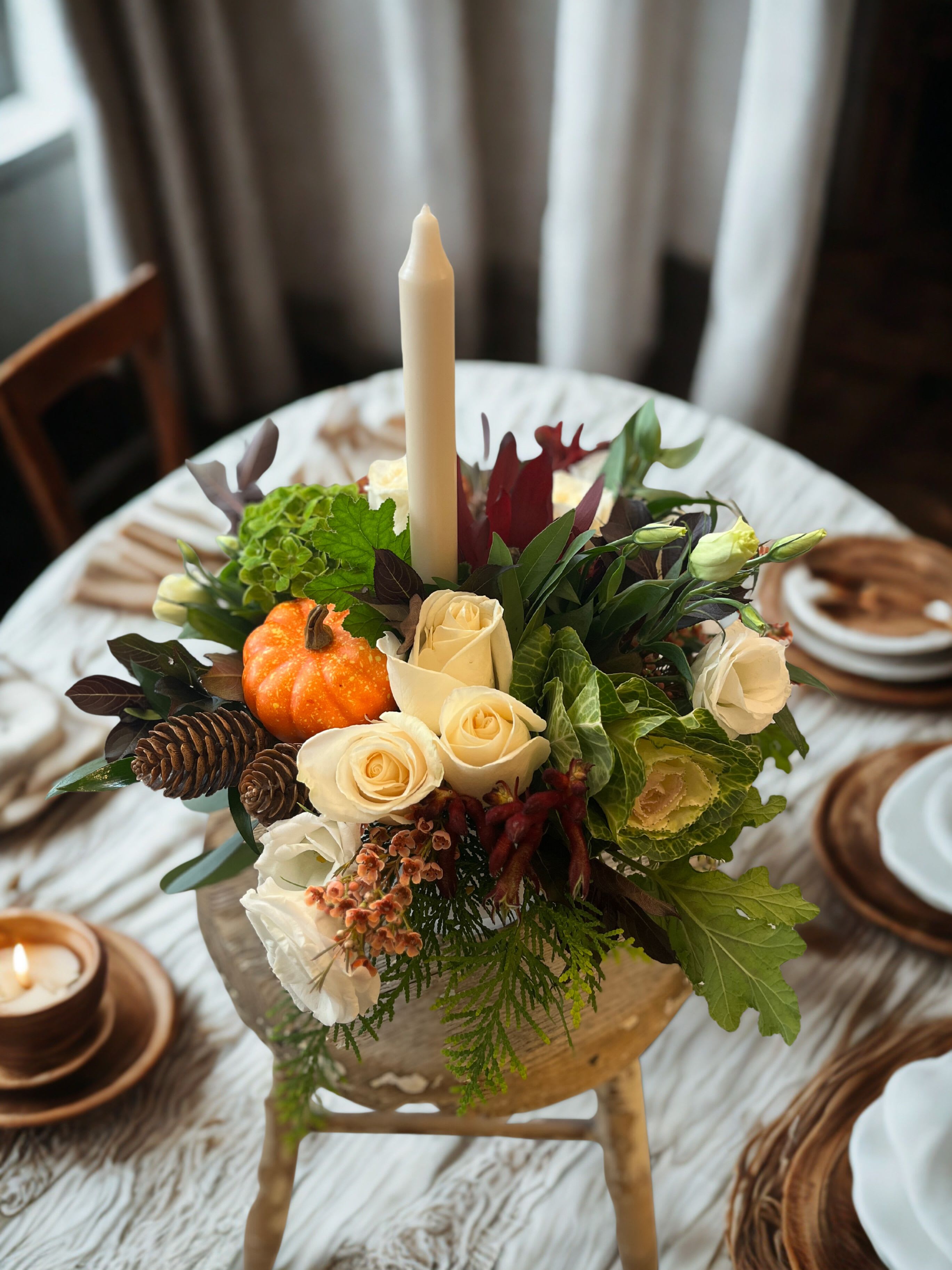 Full Abundance Centerpiece  - This round and full centerpiece is a wonderful addition to your holiday table. Send it along to your host or order for your own home! This assortment features flowers in shades of rust, burgundy and ivory with seasonal textures along with an ivory taper candle for classic elegance.  Approx. 14x 14" with candle.   This piece is available in custom colors - please leave any instructions in the notes. 