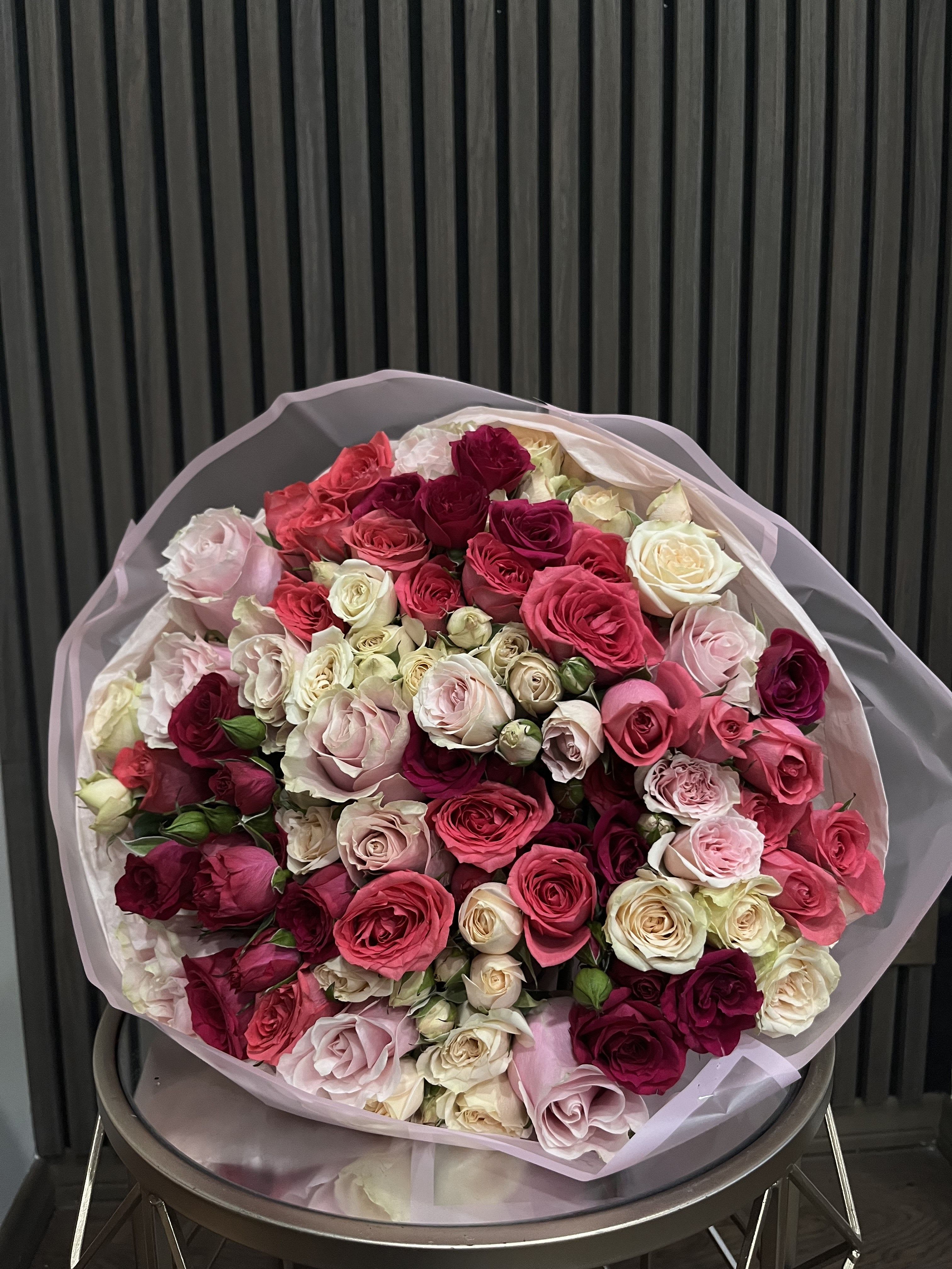 Large bouquet of pink, red, and cream roses wrapped in pale paper