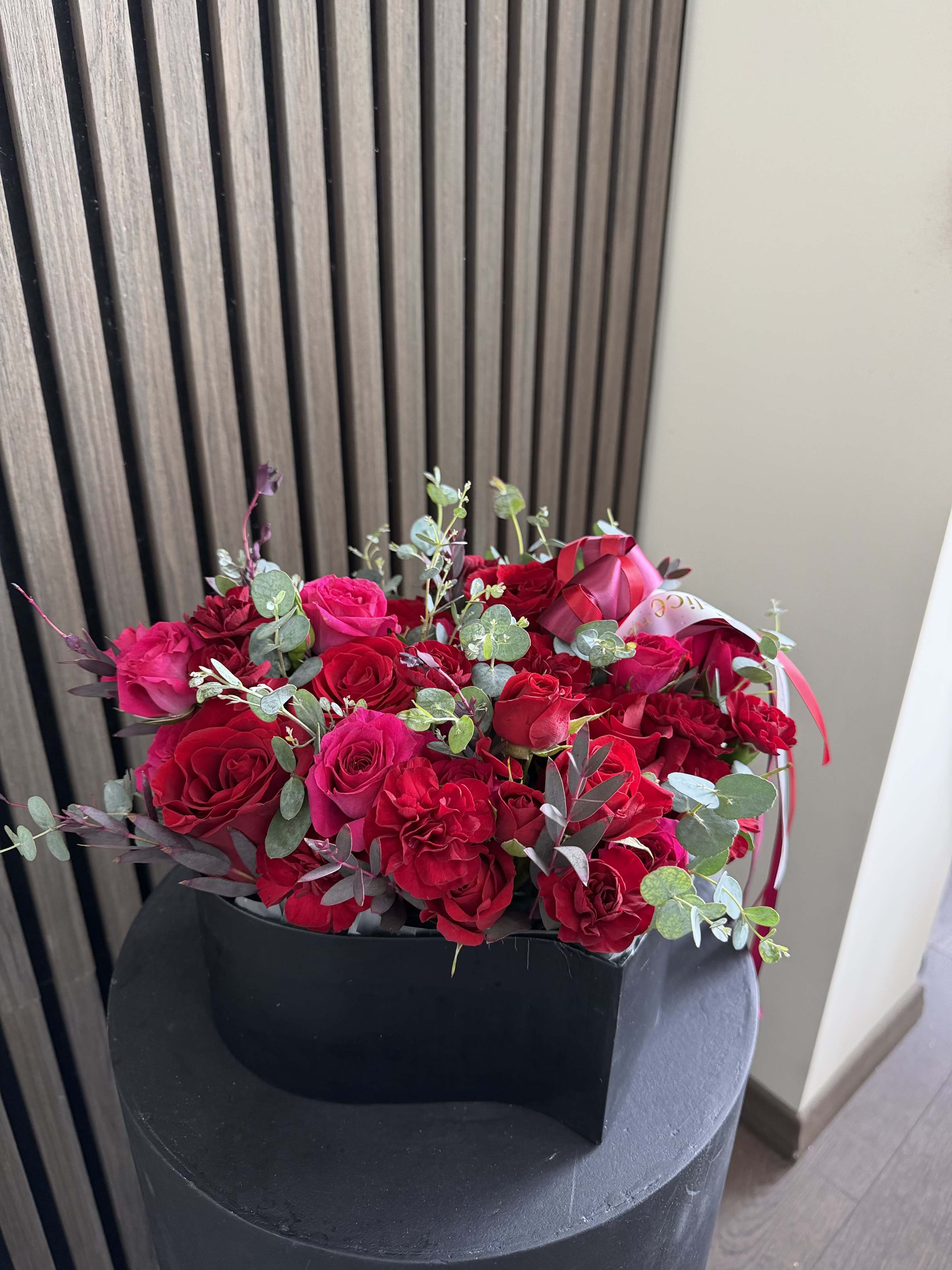 Red Velvet Heart Box - A timeless and luxurious heart-shaped flower arrangement featuring rich red roses and premium red blooms, accented with fresh eucalyptus for a modern, elegant touch. This design embodies deep love, passion, and sophistication. The bold red palette combined with the structured heart shape creates a powerful romantic statement — perfect for making unforgettable impressions. Arranged in a sleek premium box, this piece is both classic and contemporary, ideal for high-end gifting. Perfect for Valentine’s Day, Anniversary, Love and Romance, Proposal, and Special Occasions. Please note: due to seasonal availability, some flowers may be substituted. However, the heart shape, red color palette, size, and luxurious style will remain consistent with the photo. Handcrafted by Felice Flowers &amp; Design.