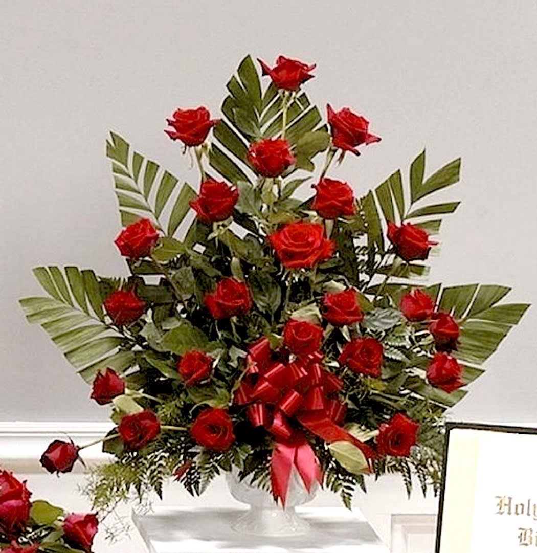 Tall arrangement of red roses with palm fronds in a white pedestal vase