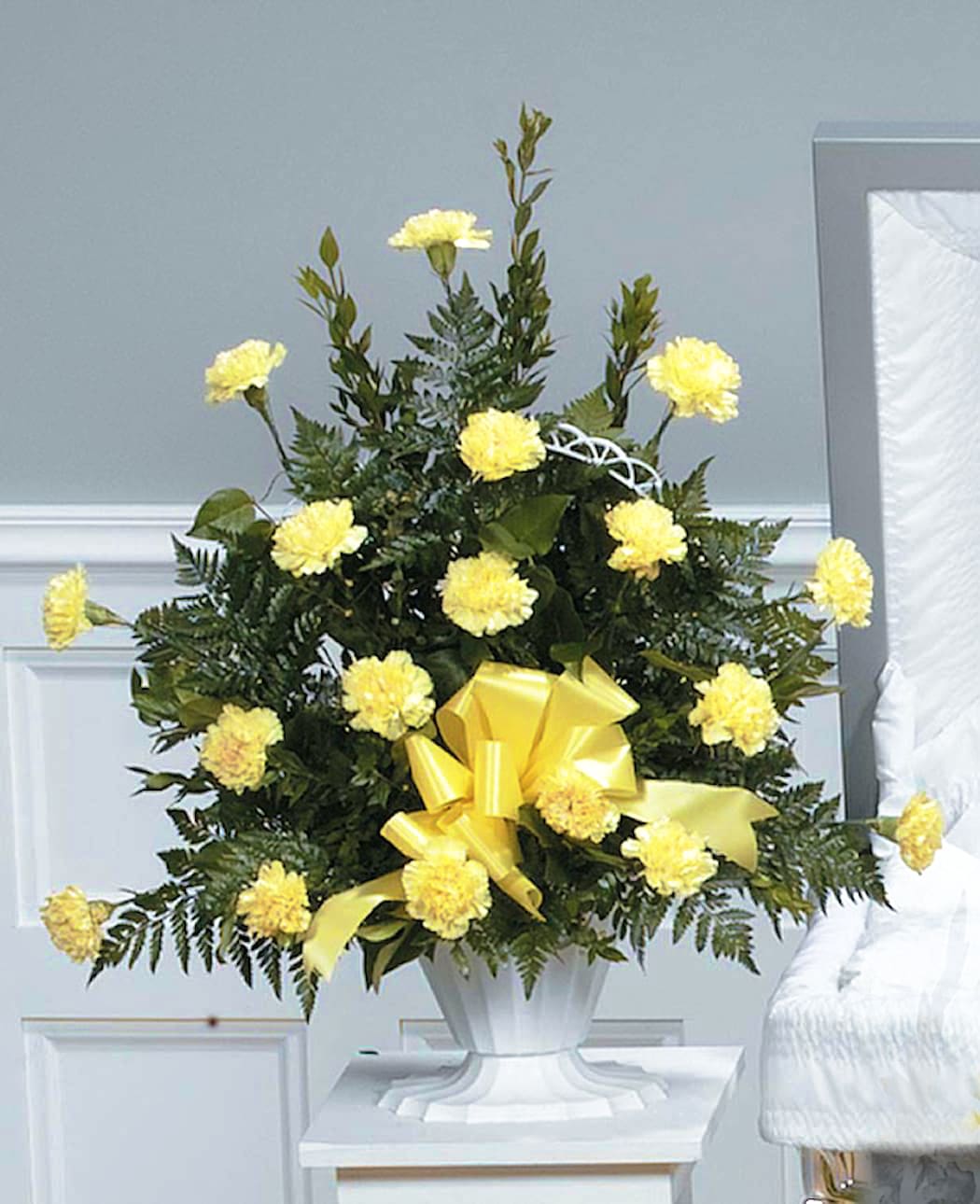 Tall arrangement of yellow carnations with a large yellow bow in a white urn vase