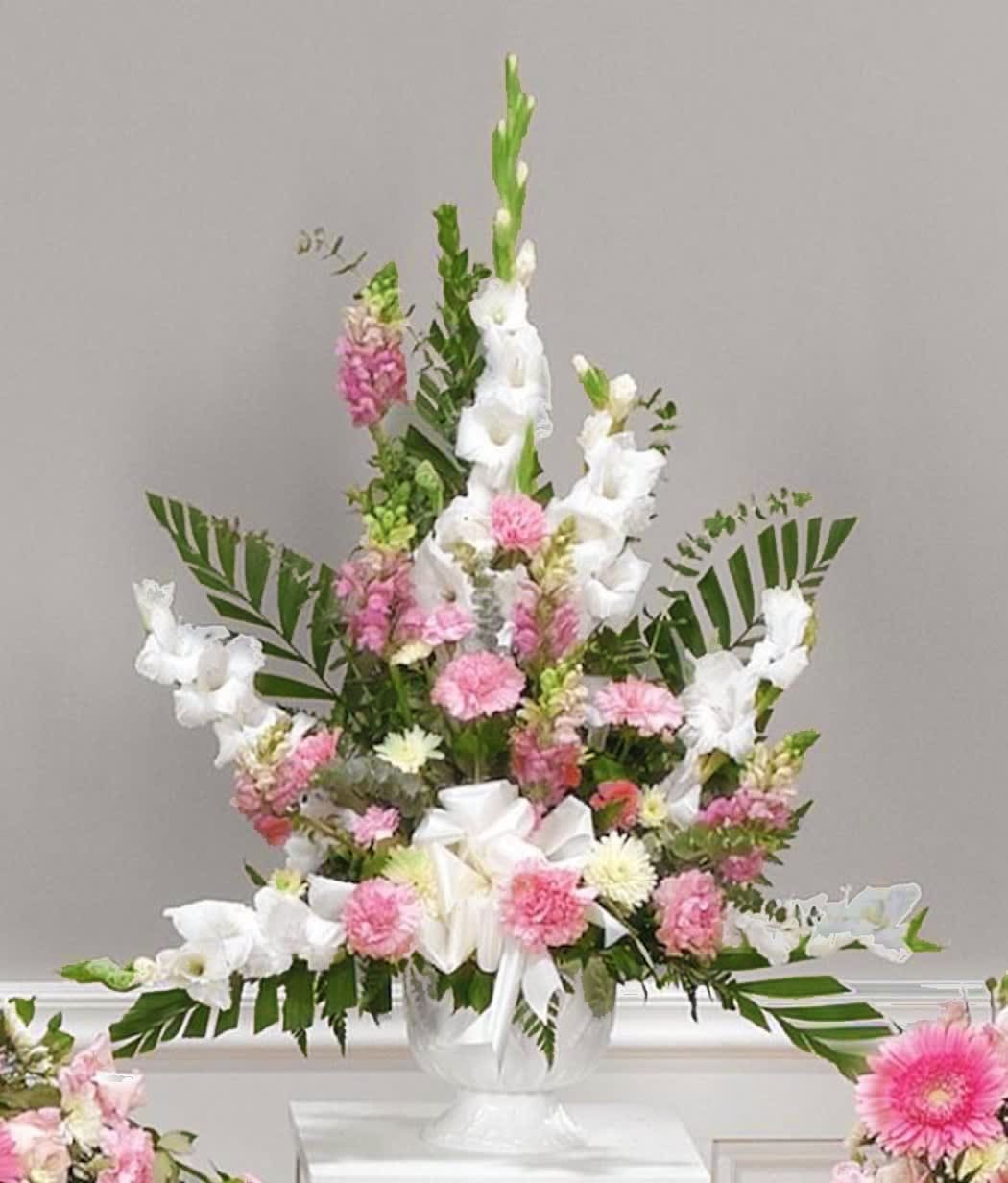 Tall pink and white arrangement with carnations and gladiolus in a white urn with a bow