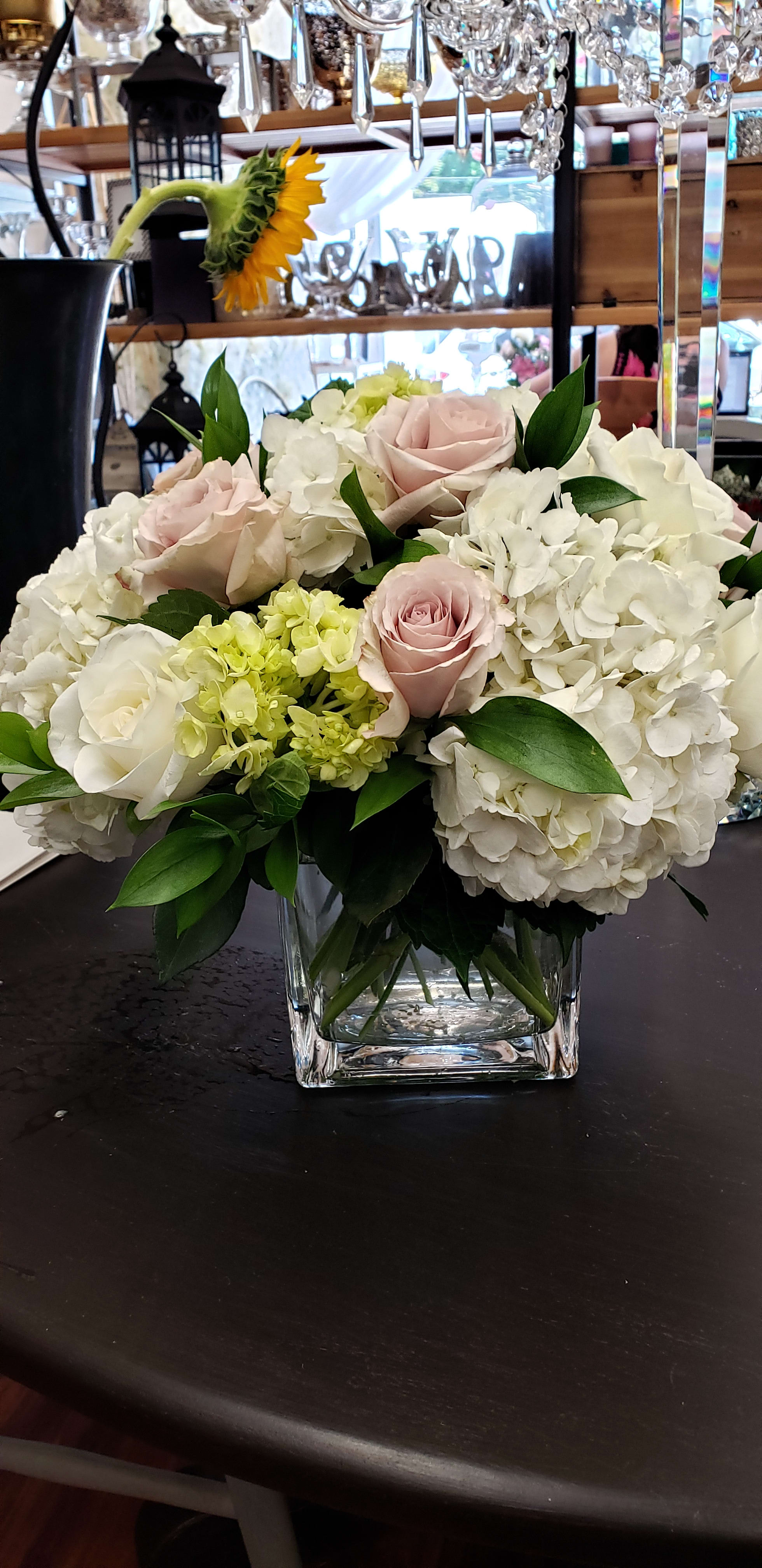 Low arrangement of white hydrangeas and blush roses in a clear glass cube vase