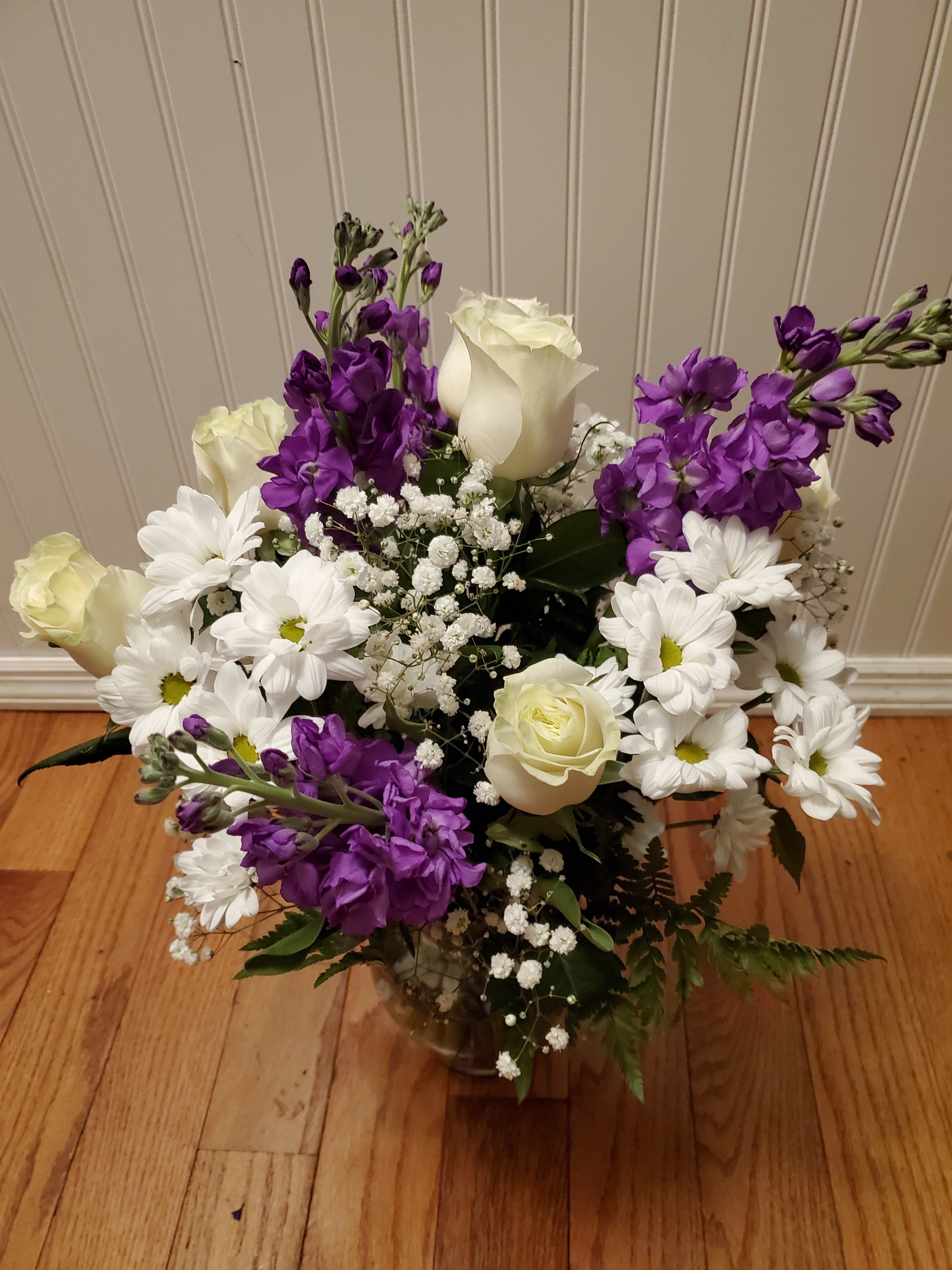 Mixed bouquet of white roses, white daisies, and purple flowers arranged in a clear glass vase