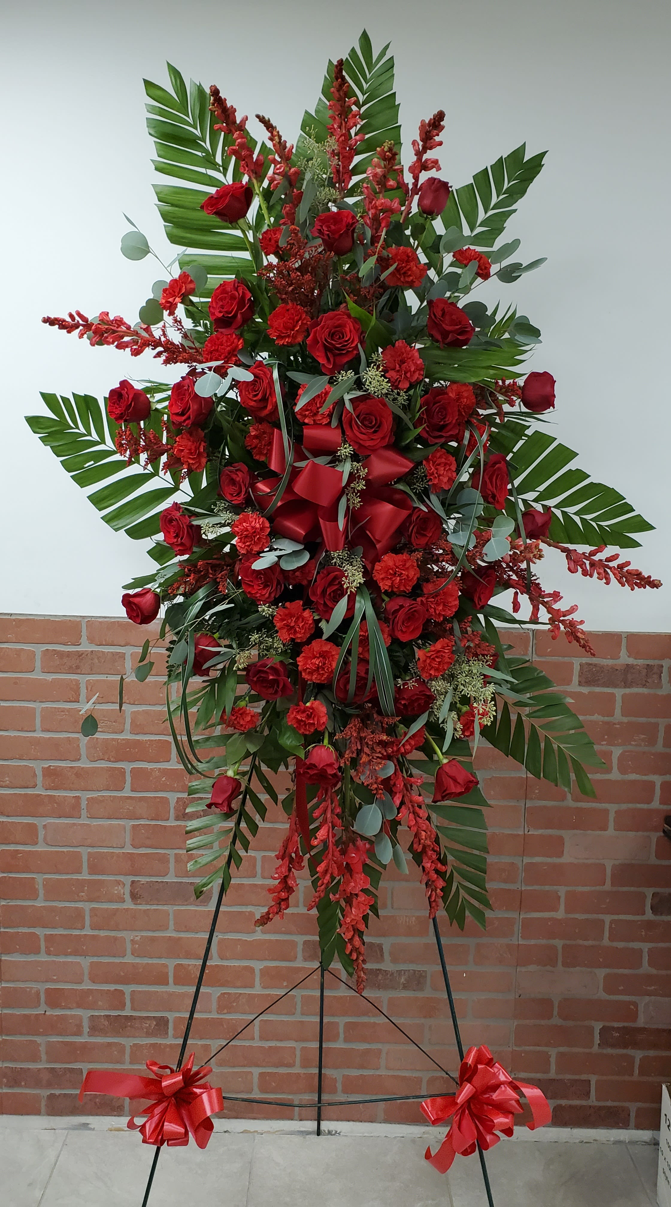 Tall red rose and carnation standing spray with palm leaves on a metal easel