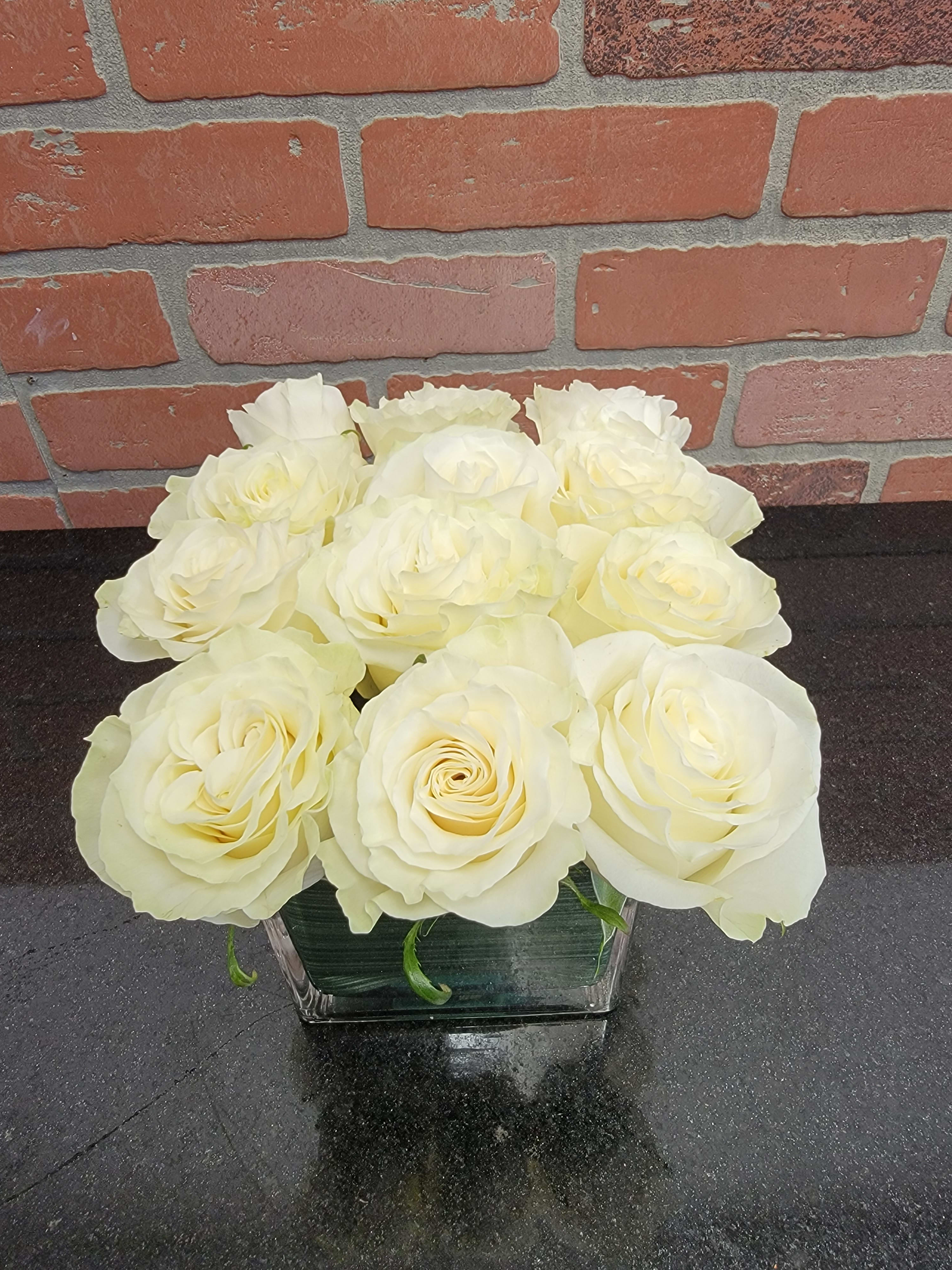 Low arrangement of pale cream roses in a square clear glass vase on a dark countertop