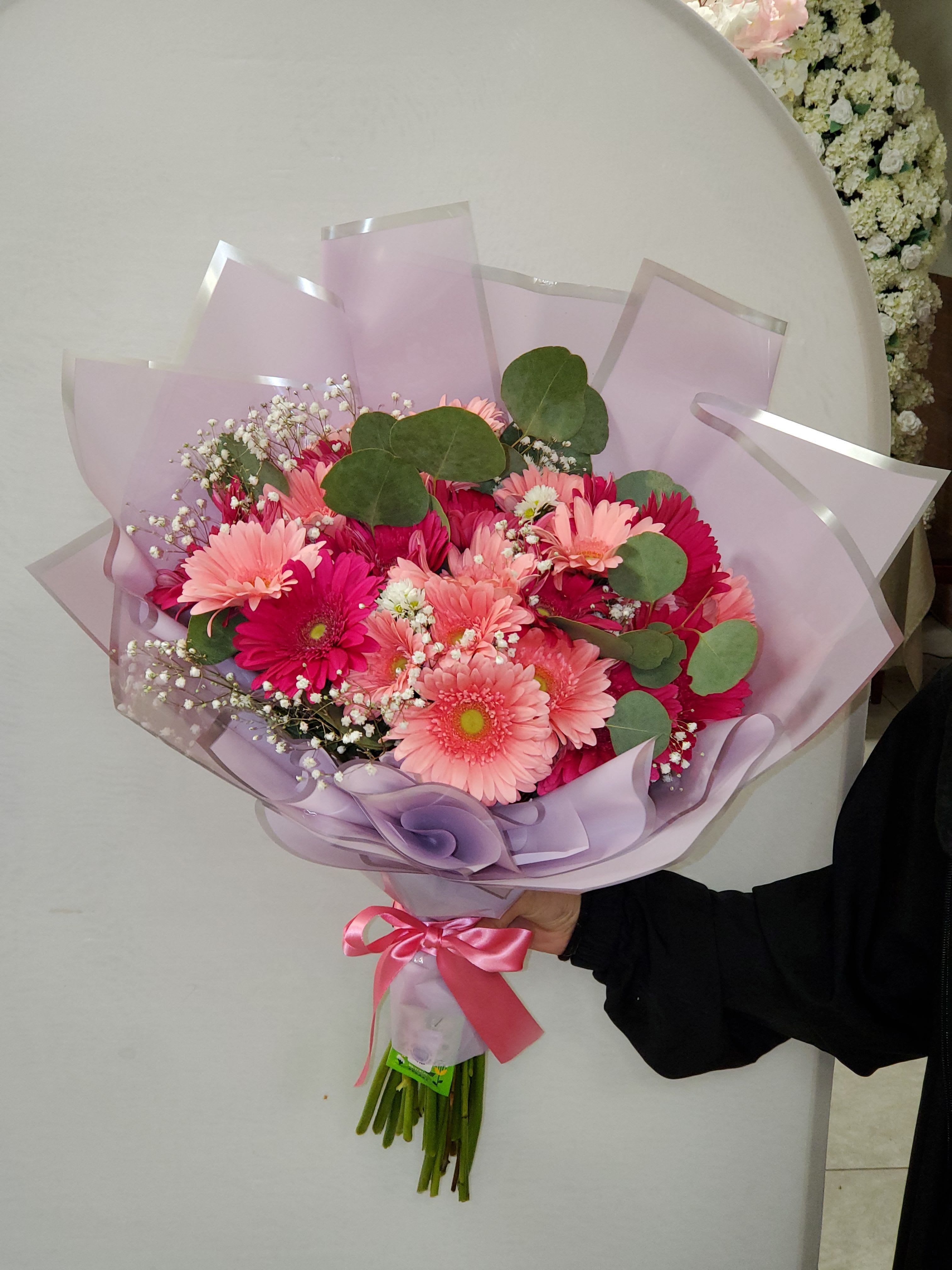 Hand-tied bouquet of pink gerbera daisies wrapped in lavender paper with a pink ribbon bow