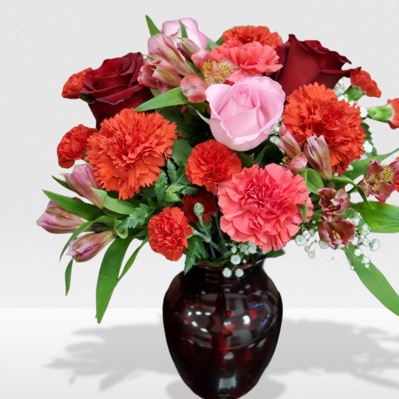 Mixed bouquet of red and pink roses and carnations in a dark red glass vase