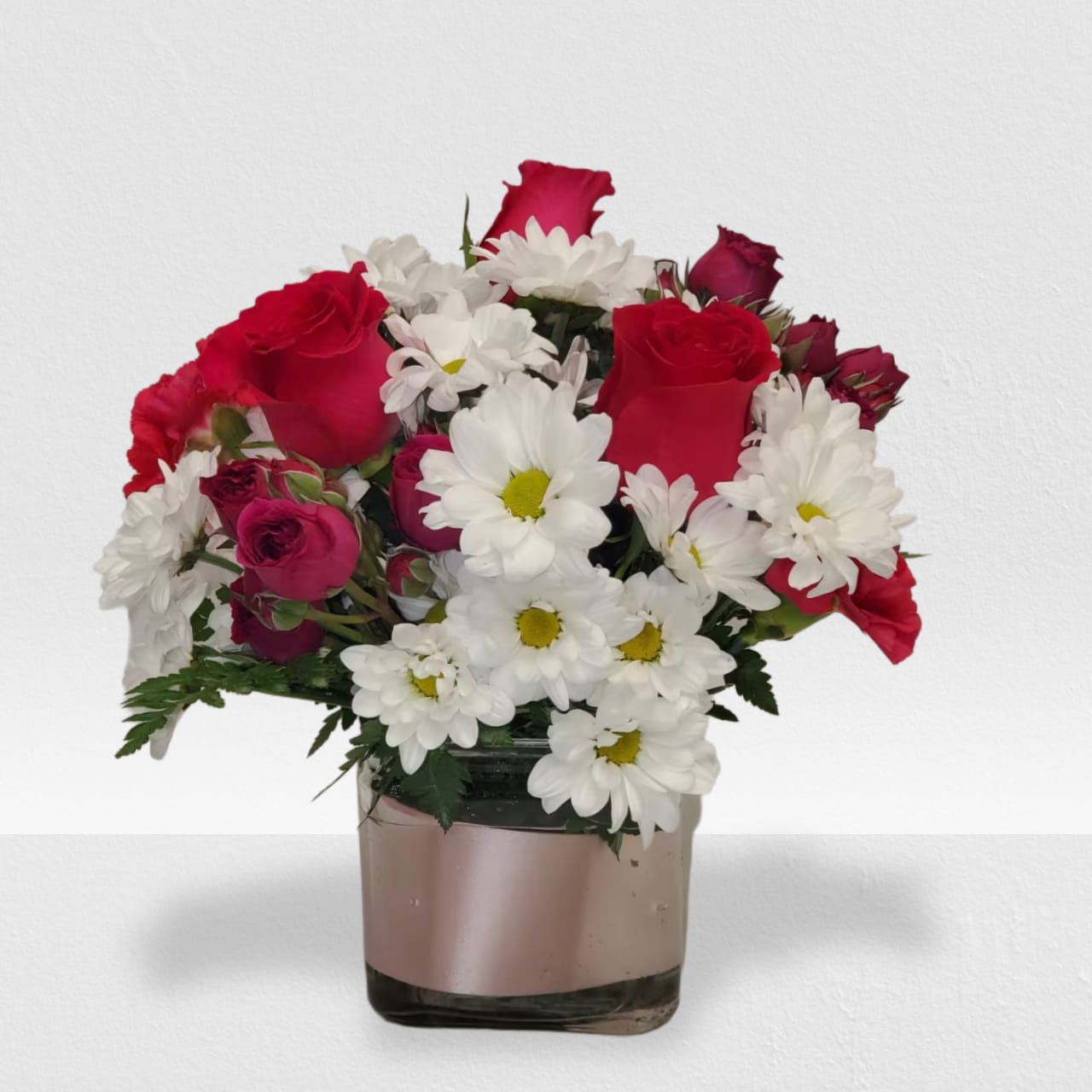 Compact red rose and white daisy bouquet arranged in a square glass vase