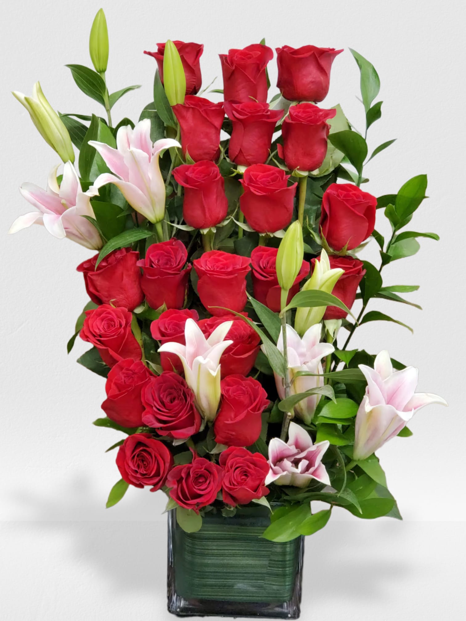 Tall arrangement of red roses and white lilies in a square glass vase